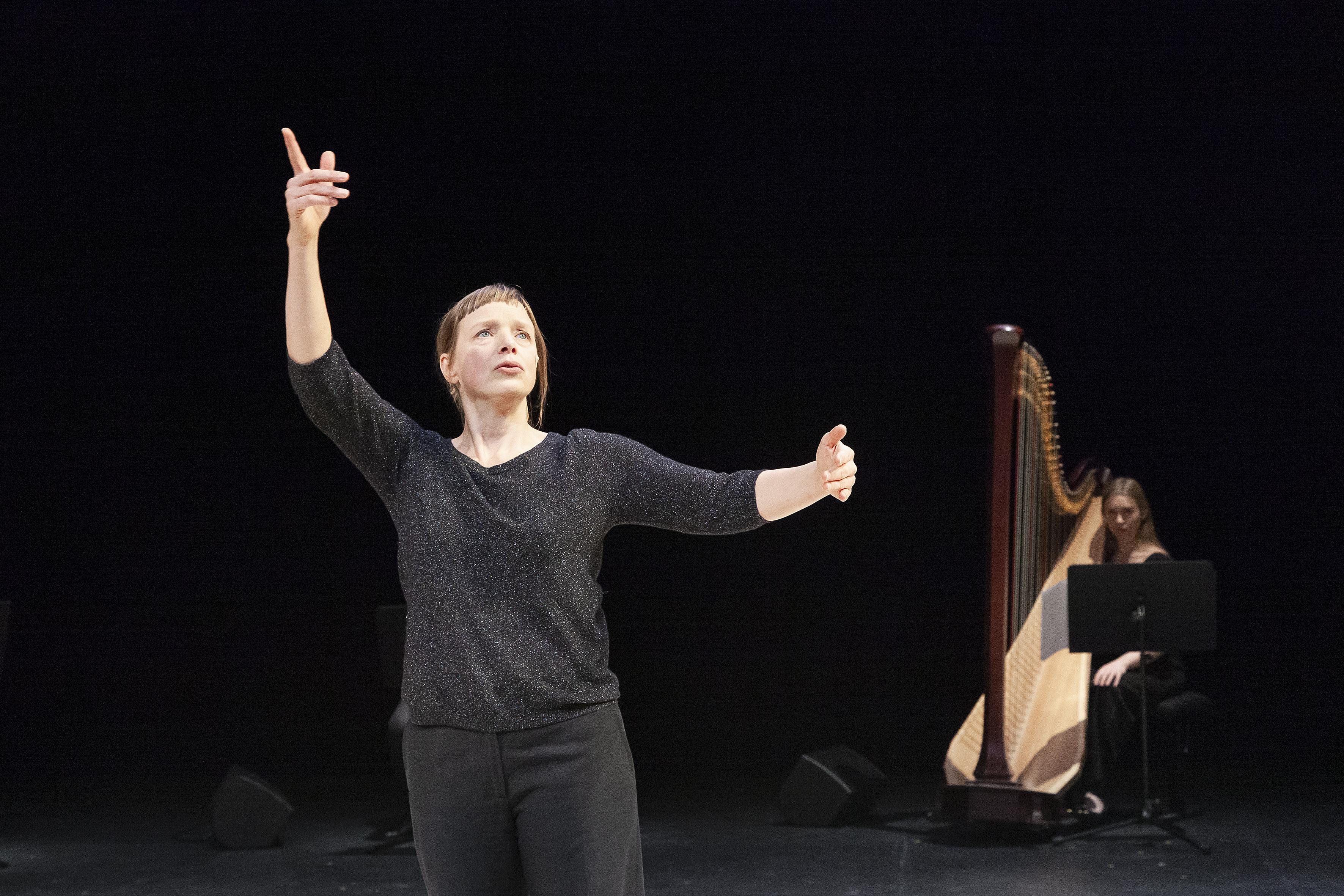 Samantha van Wissen levant les bras, devant une harpiste