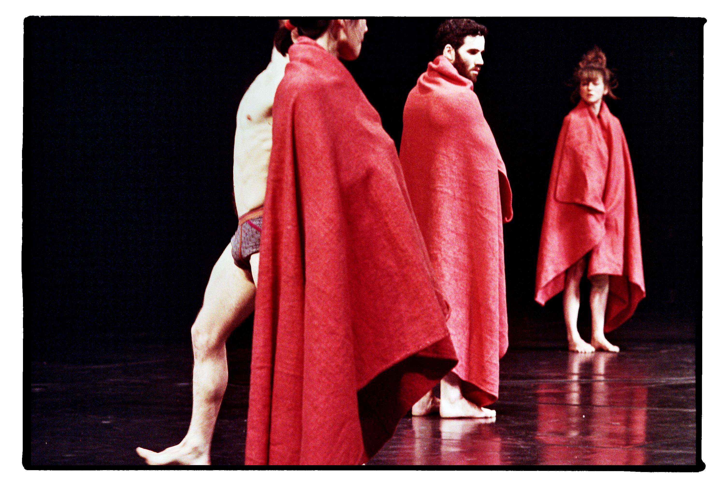 Quatre danseurs debout, dont trois sont vêtus d’une couverture rouge