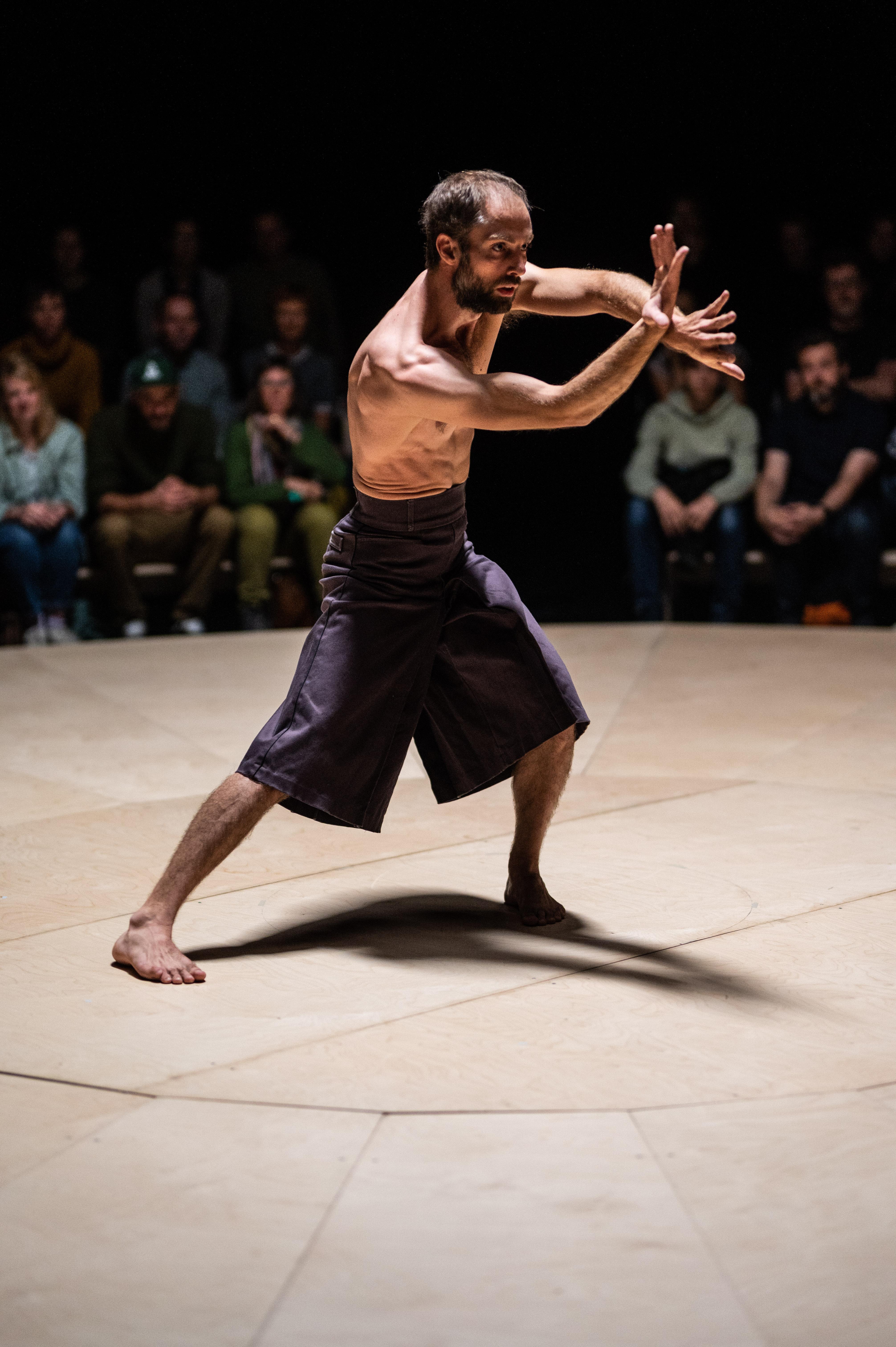 Bare-chested Alexander Vantournhout with his arms in the air, surrounded by the audience