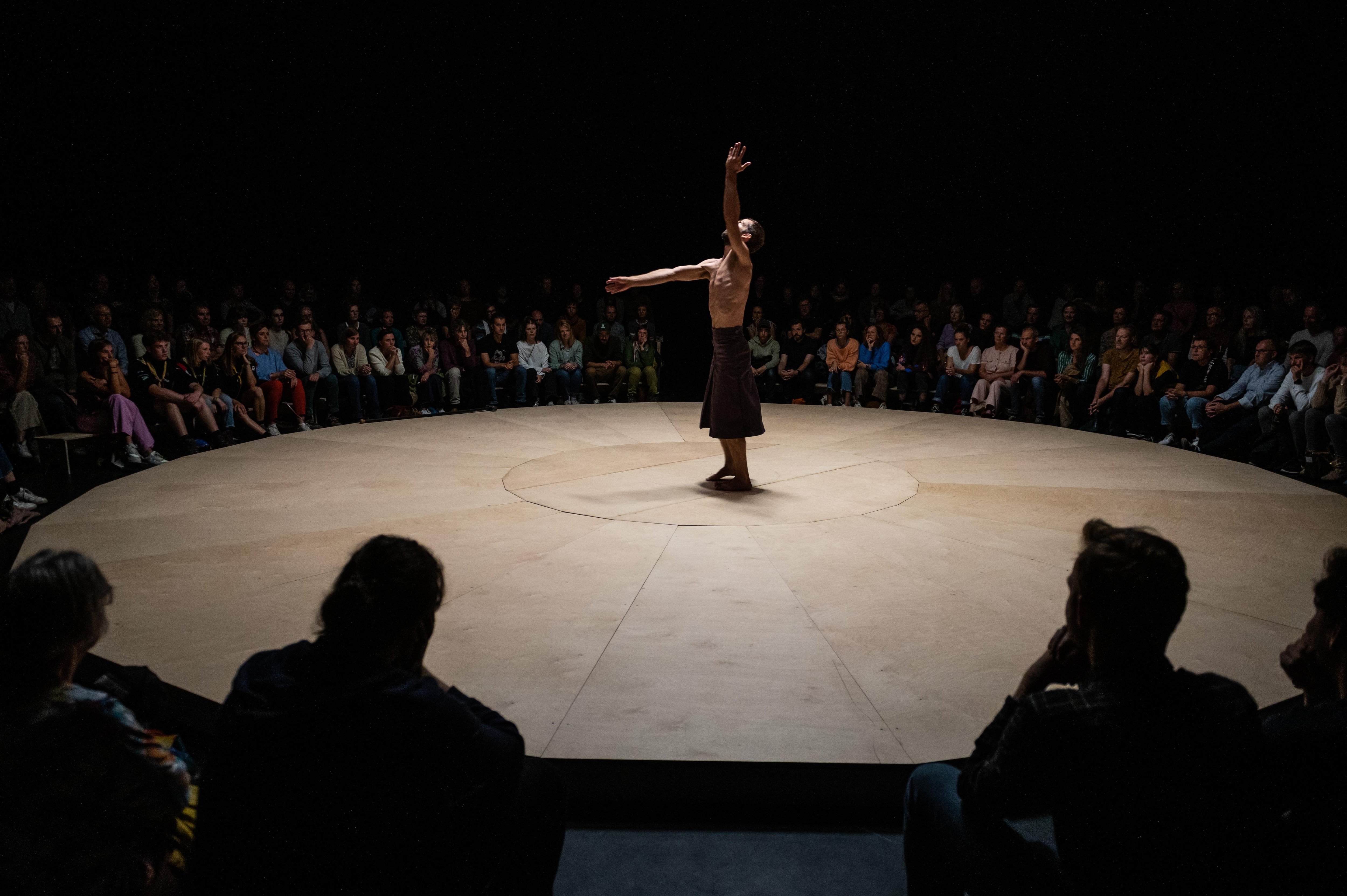 Bare-chested Alexander Vantournhout with his arms in the air, surrounded by the audience