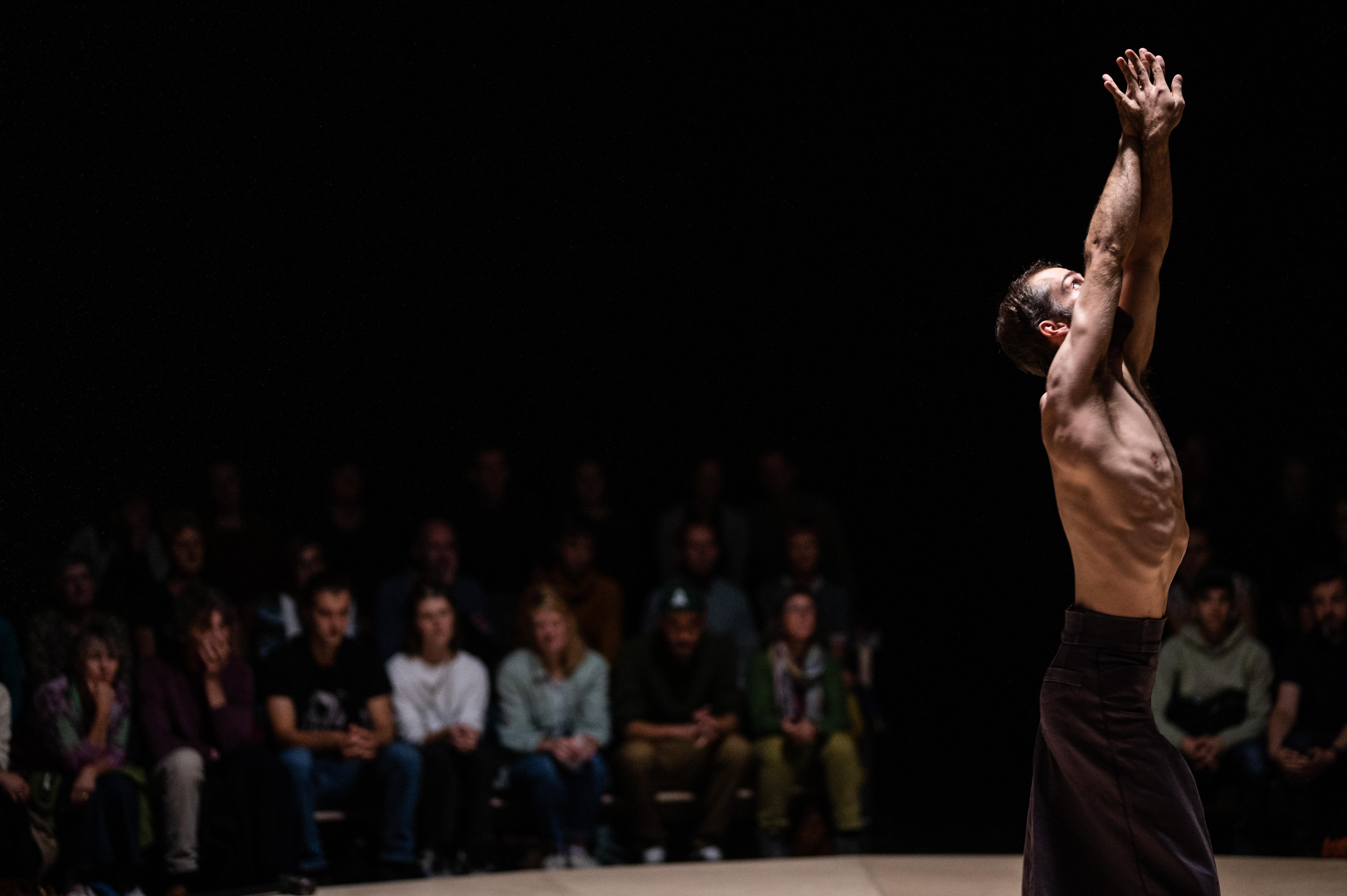 Bare-chested Alexander Vantournhout with his arms in the air, surrounded by the audience