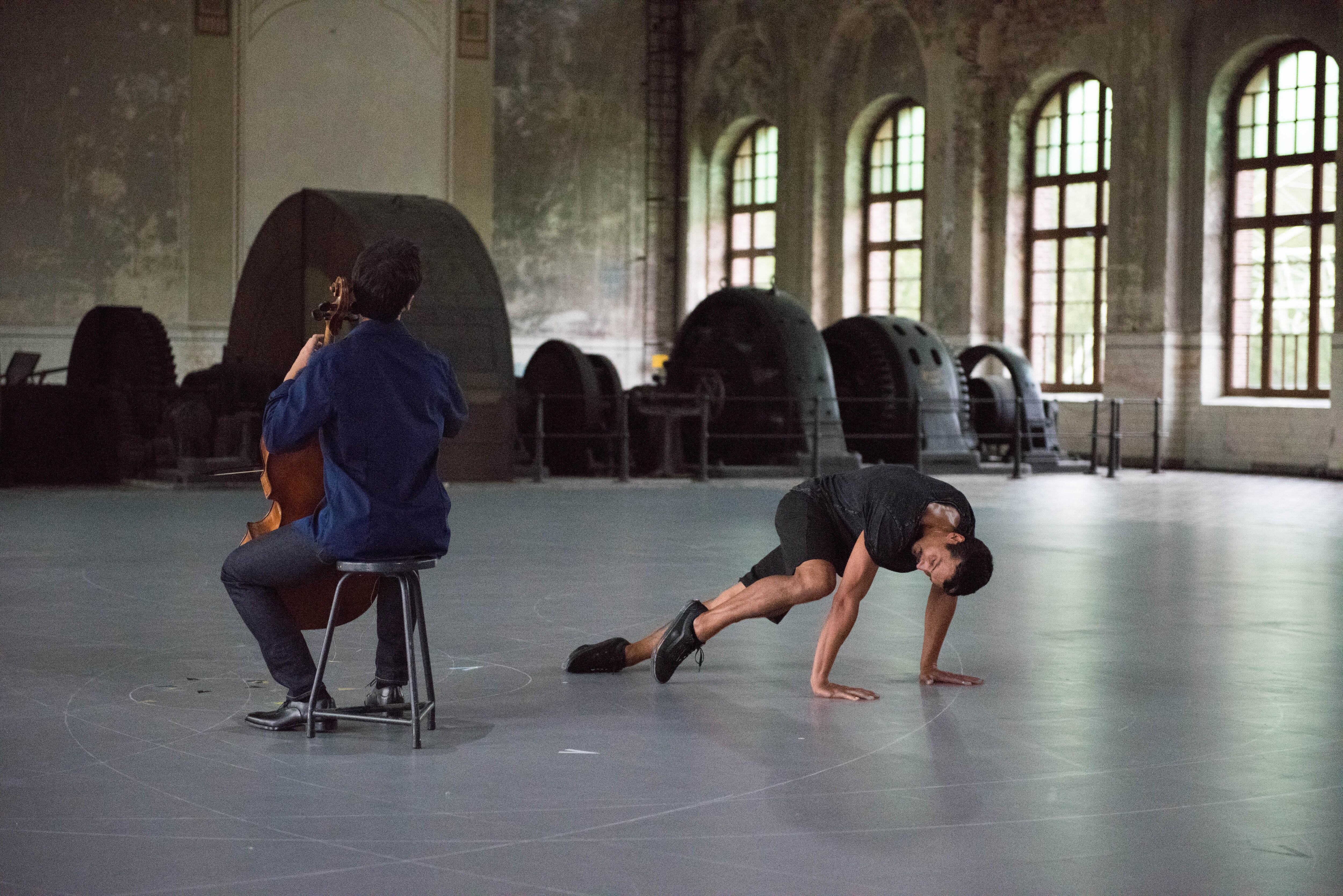 舞者双手放在地板上，旁边是大提琴家Jean-Guihen Queyras