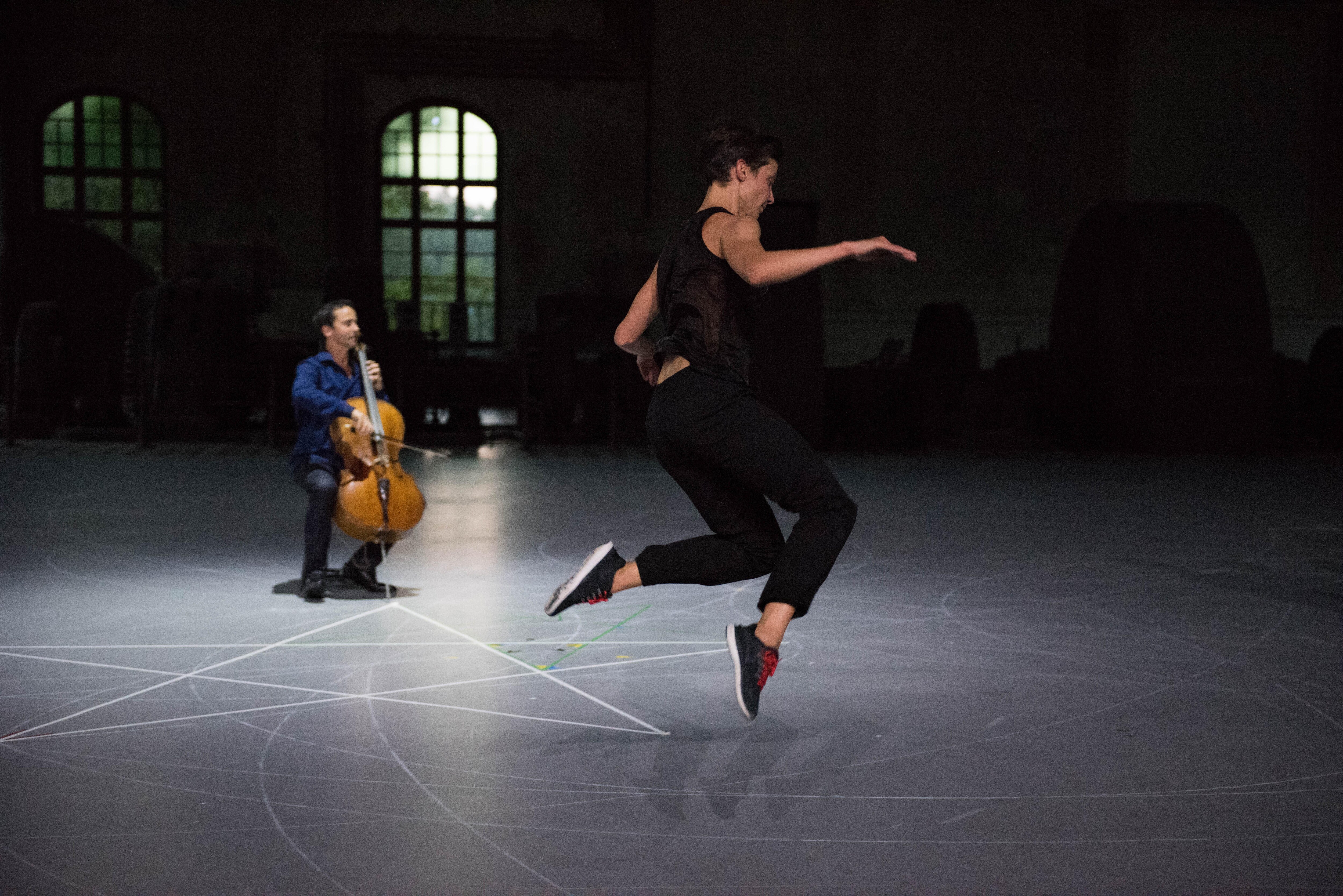 A dancer jumping in the air in front of cellist Jean-Guihen Queyras