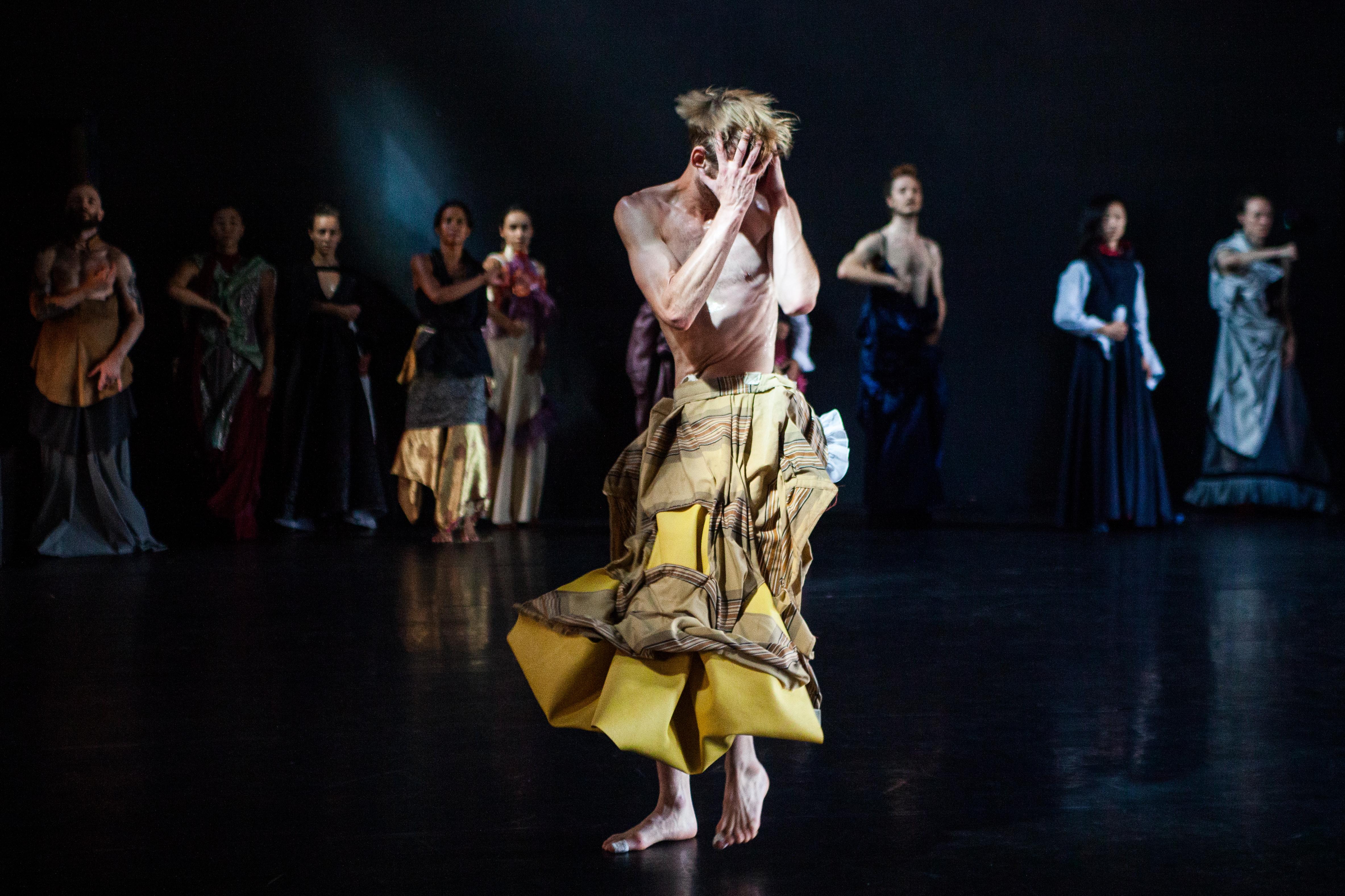 Danseur vêtu d’une jupe jaune, ses mains devant son visage