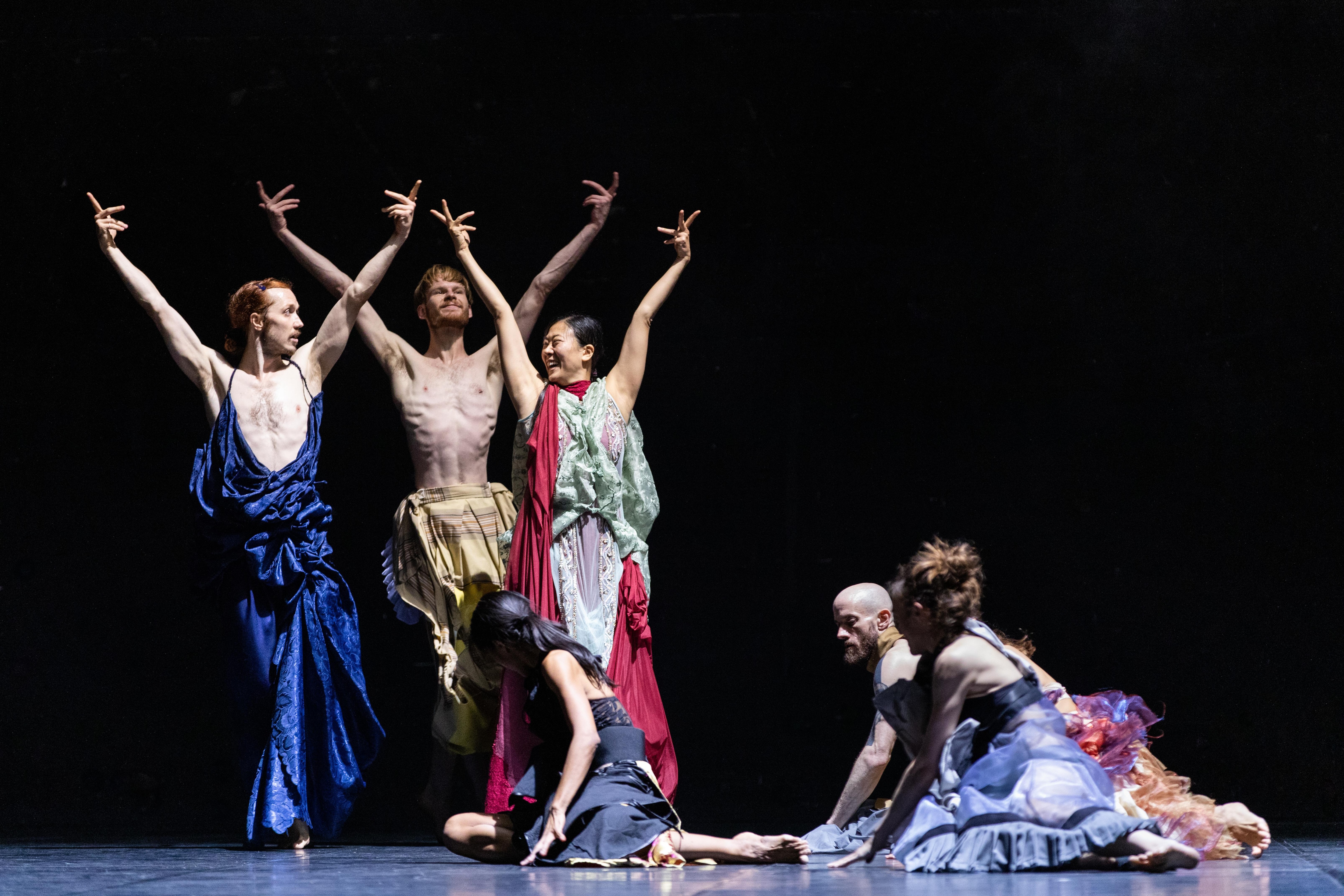 Three dancers proudly wave their hands in the air, alongside other dancers on the ground.