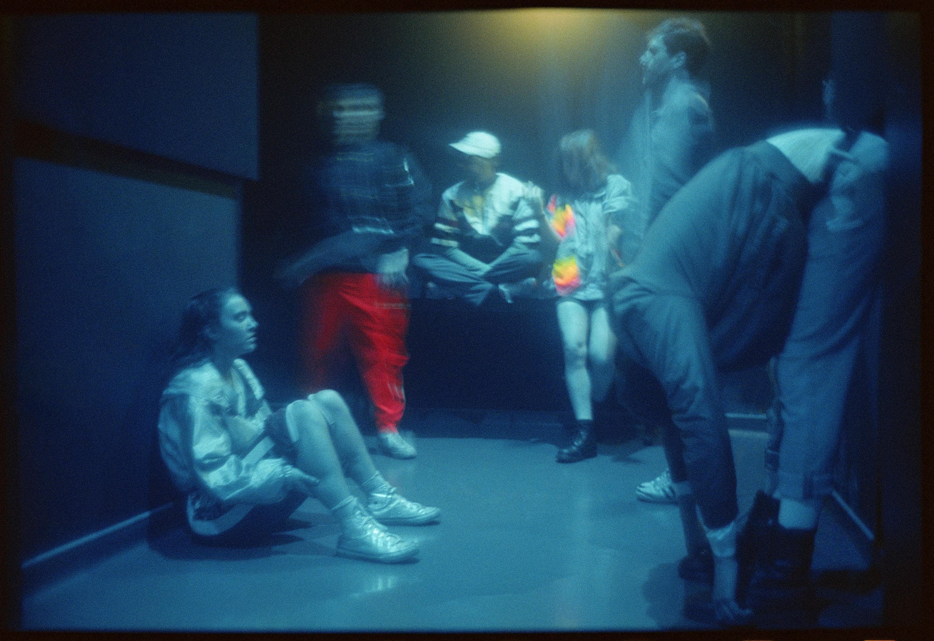 Danseurs attendant en coulisses sous une lumière bleue, assis ou s'étirant