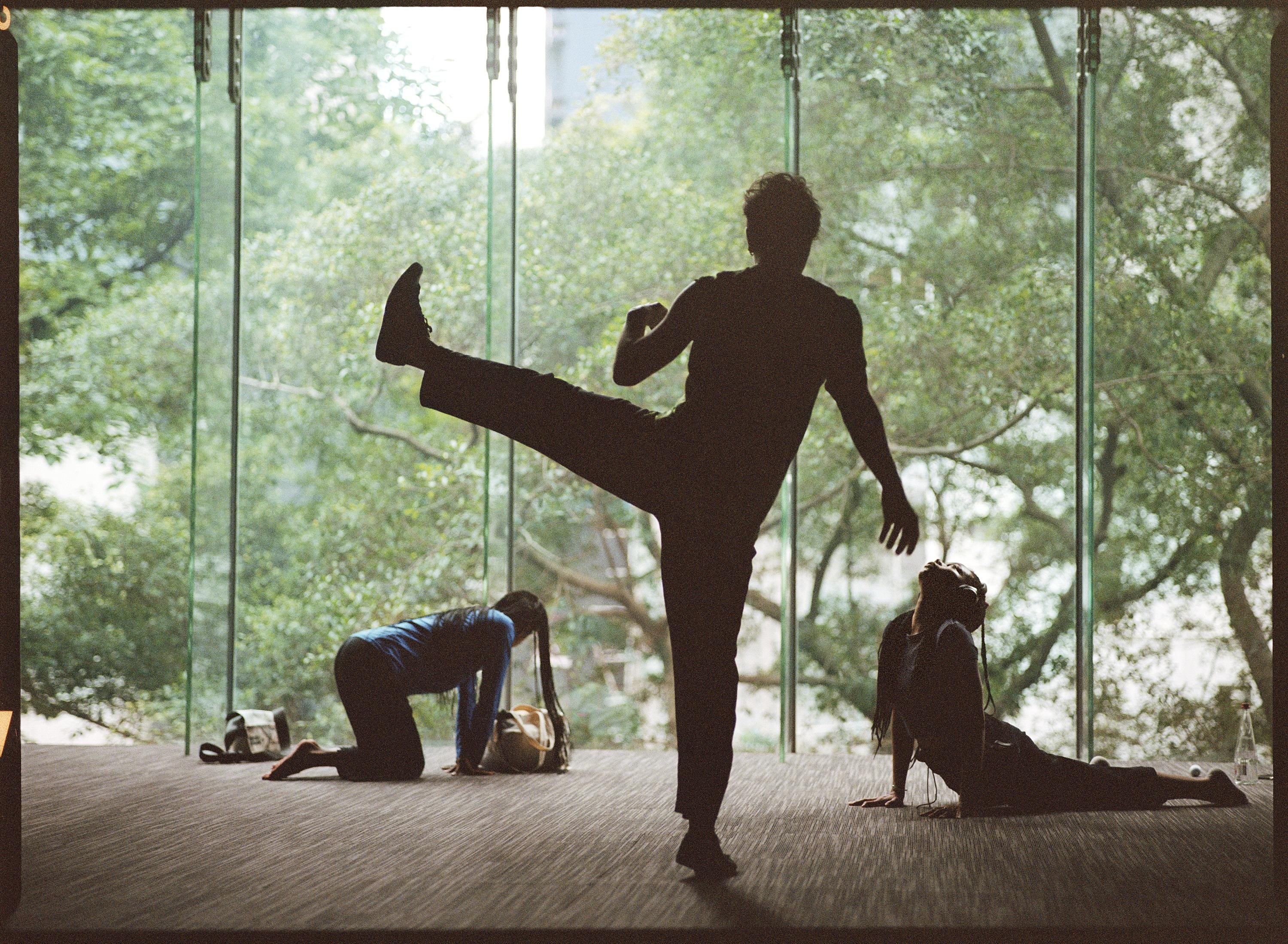 trois danseurs s'étirant dans le studio, face à la verdure derrière les baies vitrées