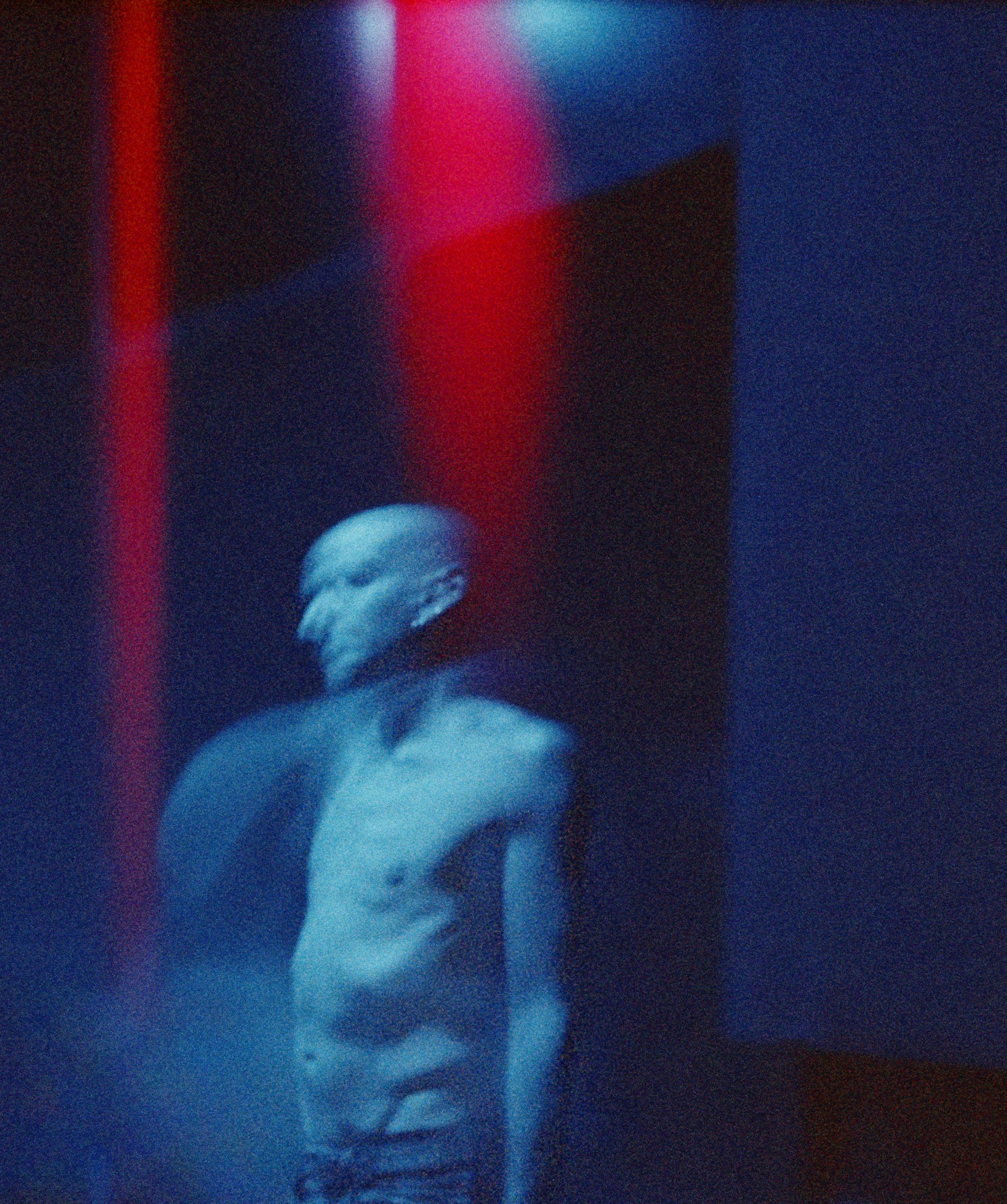 Danseur debout dans les coulisses sous une lumière bleue avec des reflets rouges
