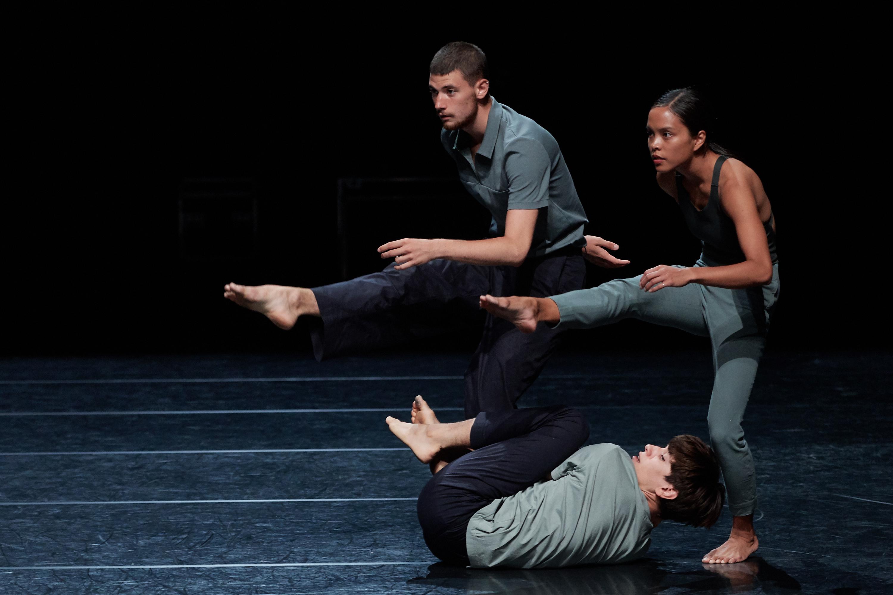 Deux danseurs debout, une jambe tendue, un troisième danseur en dessous au sol. 