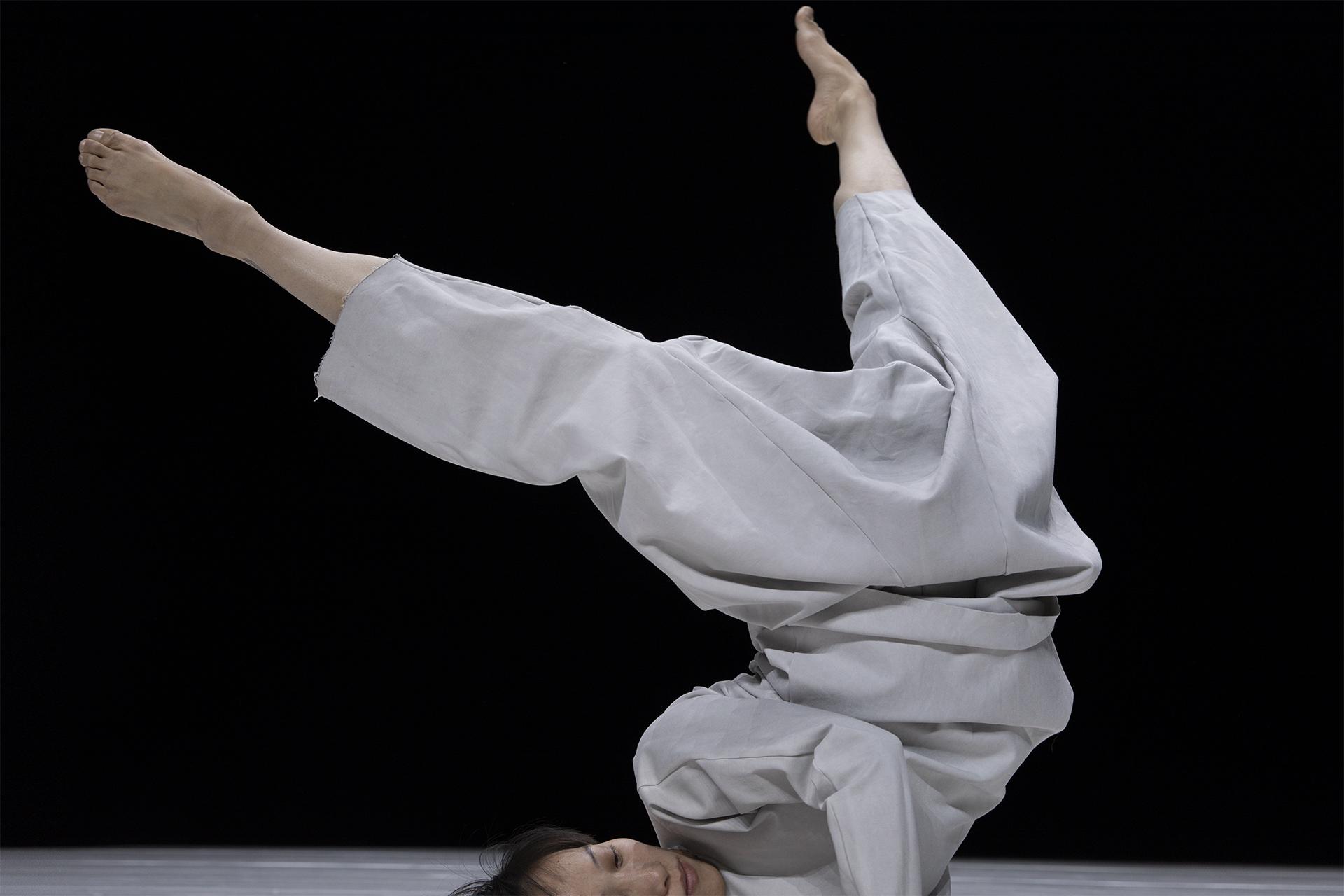 Dancer doing a headstand, in a grey ensemble