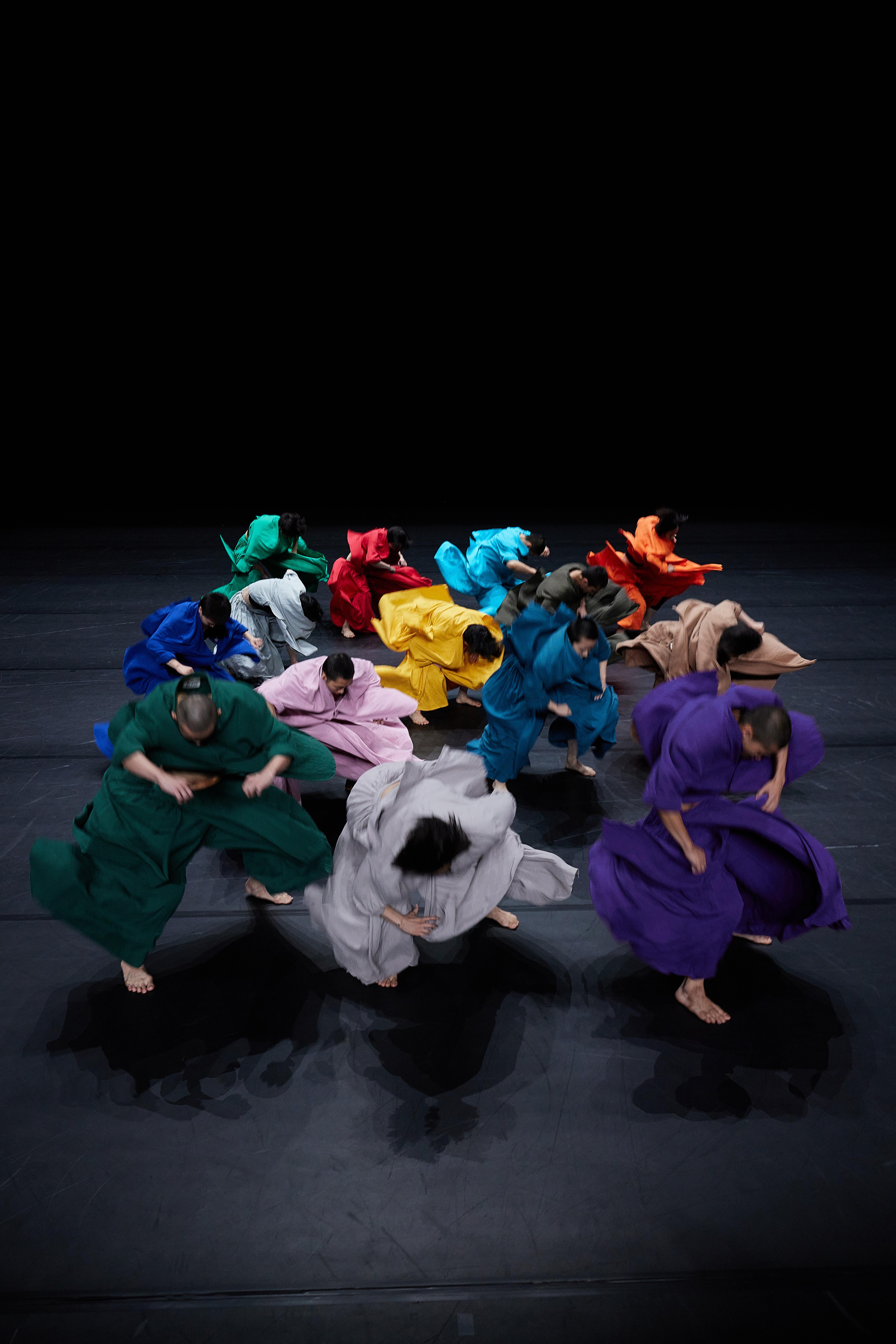 group of dancers moving in large colored jumpsuits