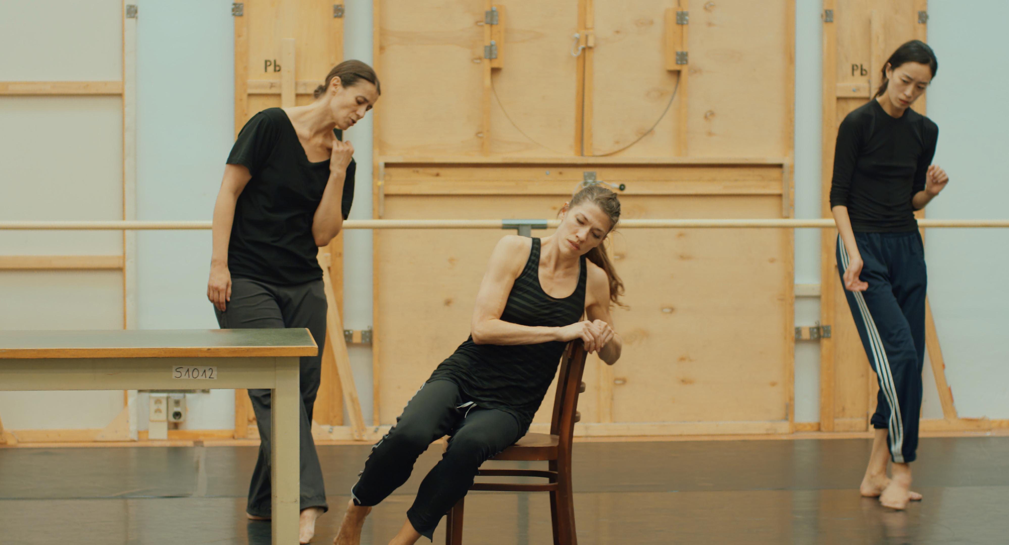 Dancers in motion in a dance studio, two standing and one seated.