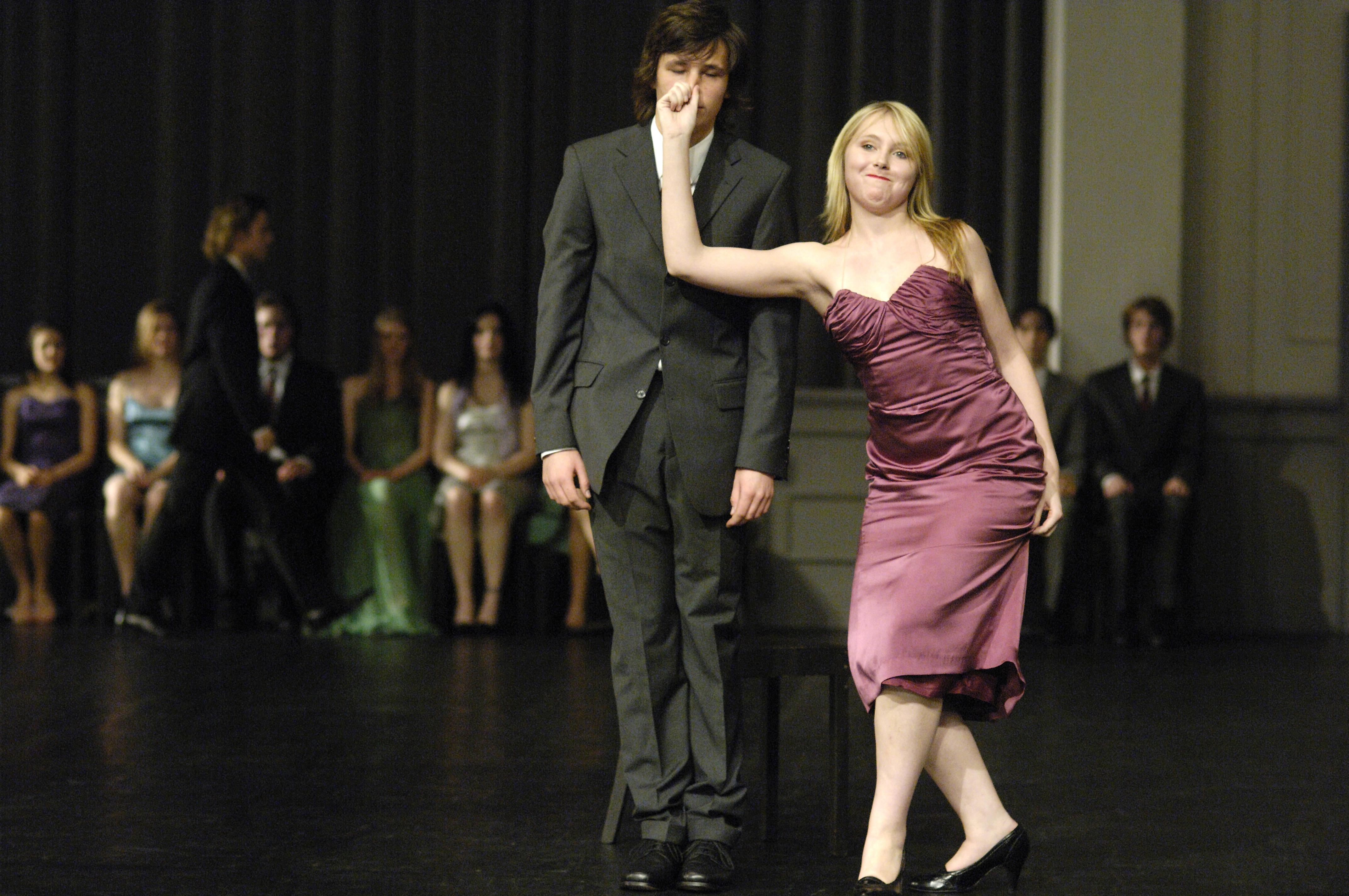 A man in a suit gets his nose pinched by a woman in a purple evening gown.