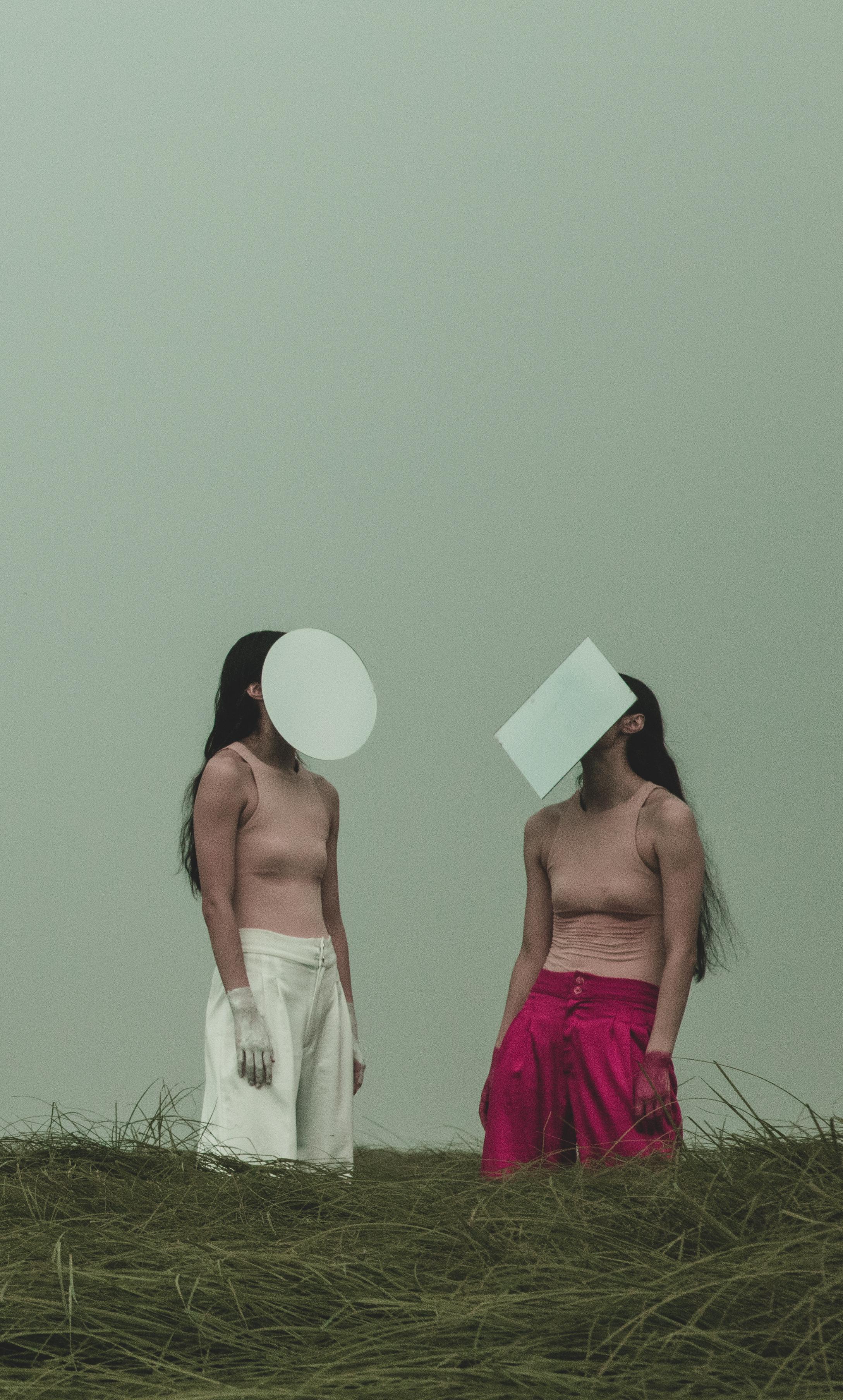 兩名穿背心的女子，一名以一張圓形的紙遮臉，另一名以一張長方形的紙遮臉。