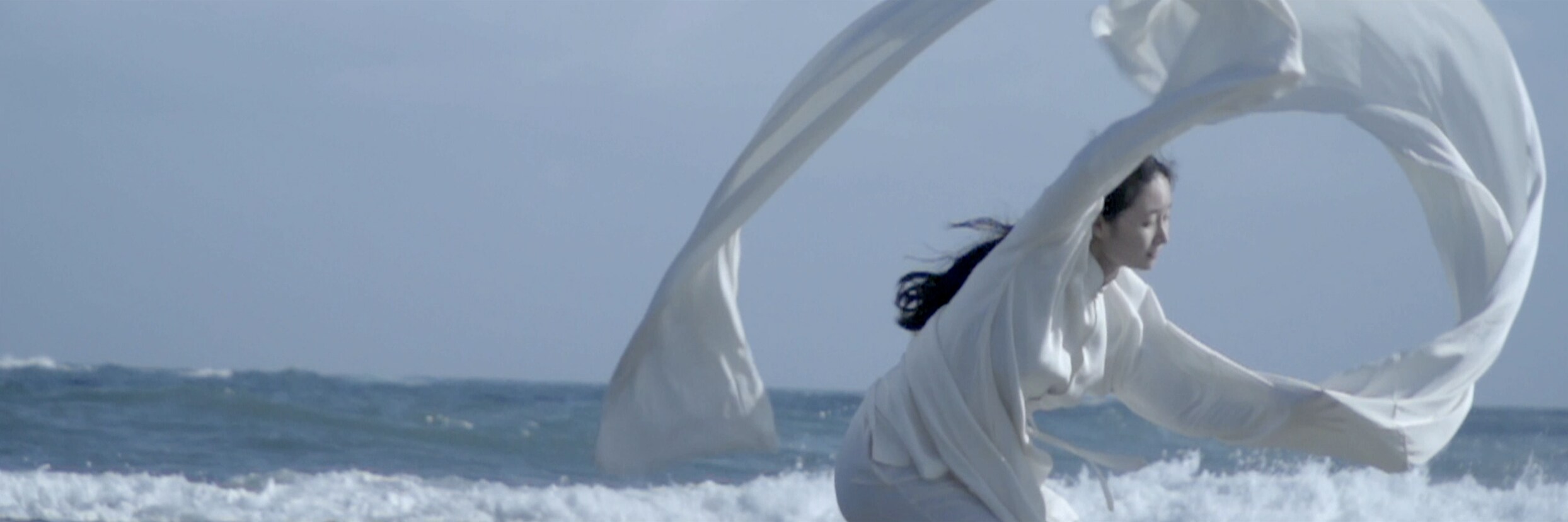 woman flying a large white cloth by the sea.