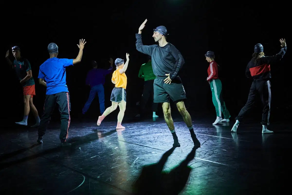 moving dancers on stage with bathing caps and swimming goggles on their heads