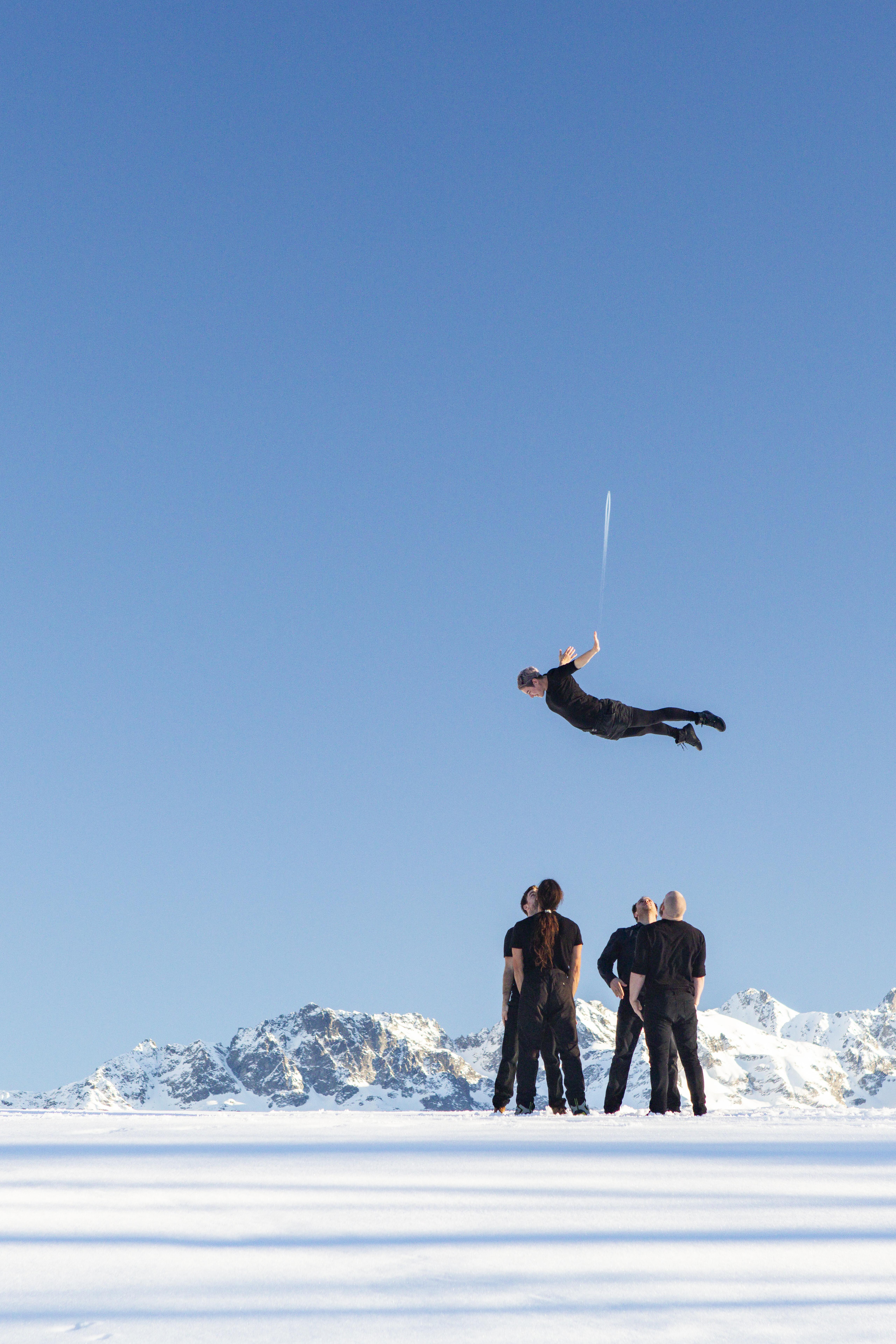 Four men in black catch a fifth man in mid-air in the snow.