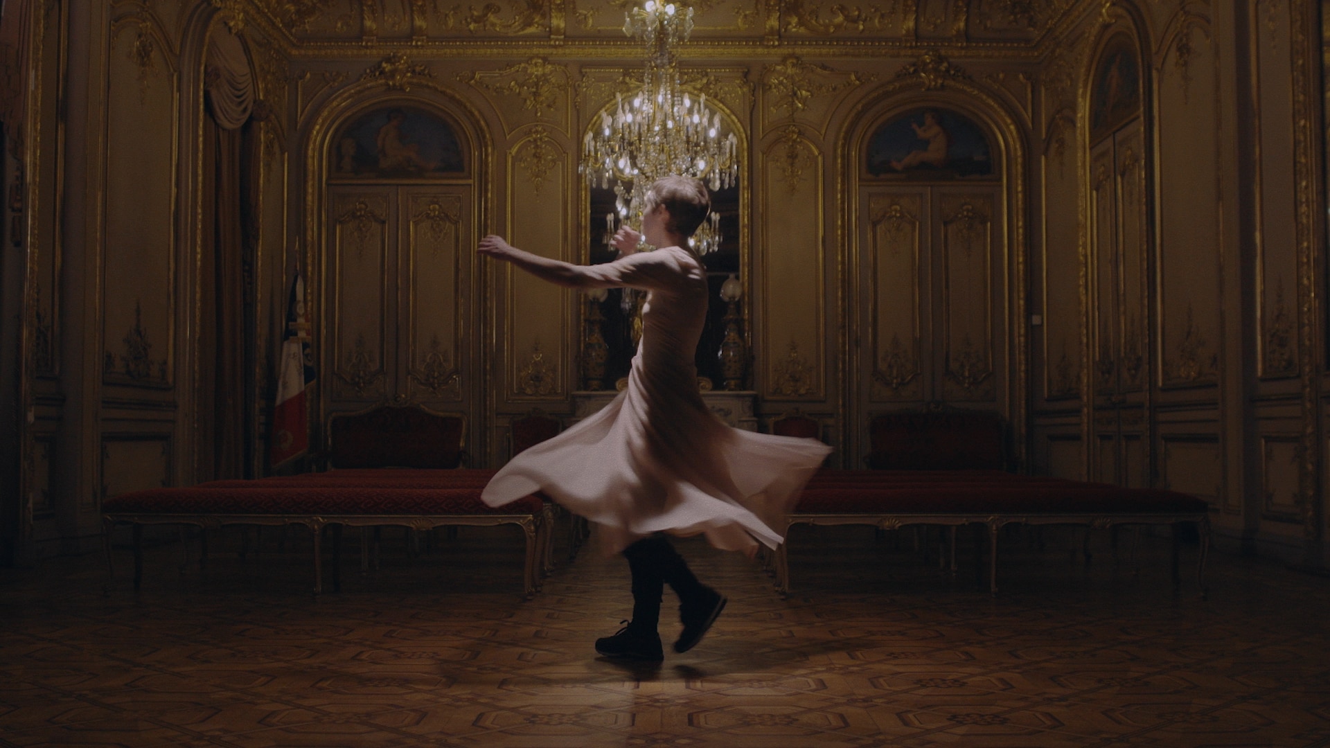 Dancer turning in a dress in the middle of a room with a large chandelier.