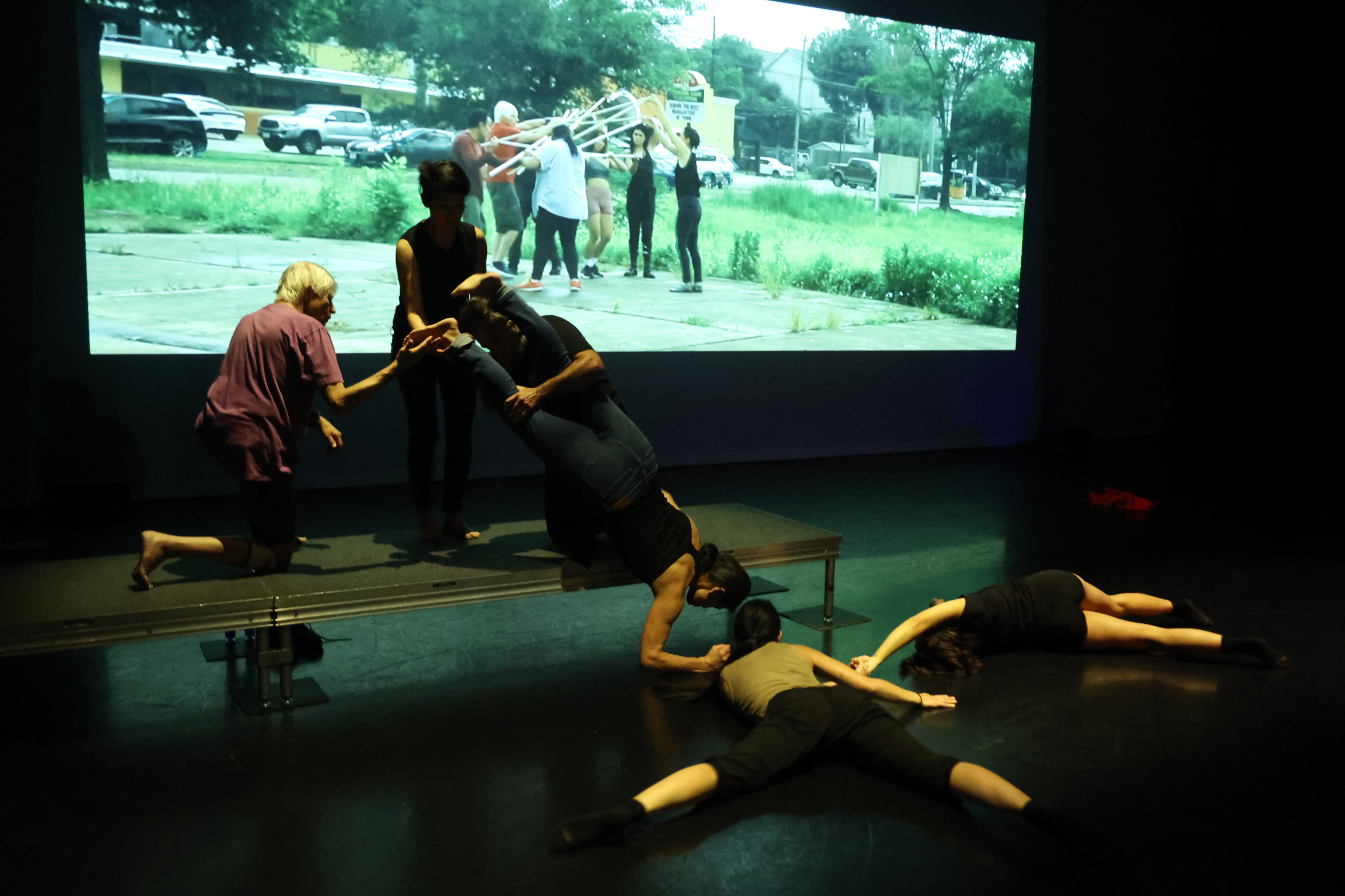 Dancers lying on the floor and on a bench - video in the background.