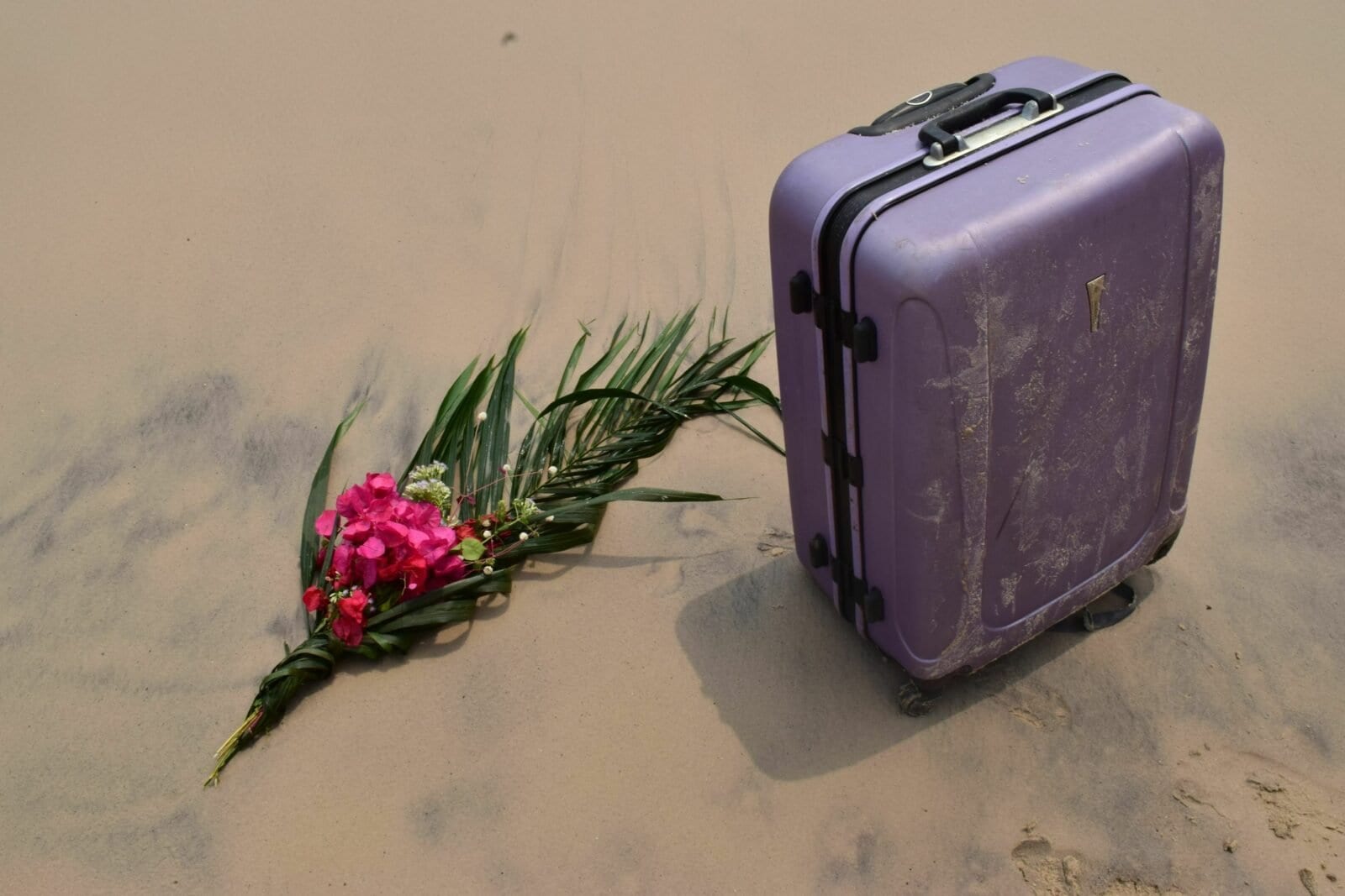 Une valise et un bouquet de fleurs sur le sable.