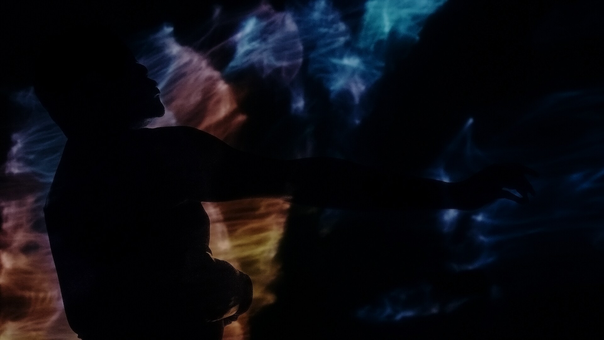 Jaamil, bras tendu vers l’extérieur, se dessine en ombre contre un fond de réfractions lumineuses colorées.