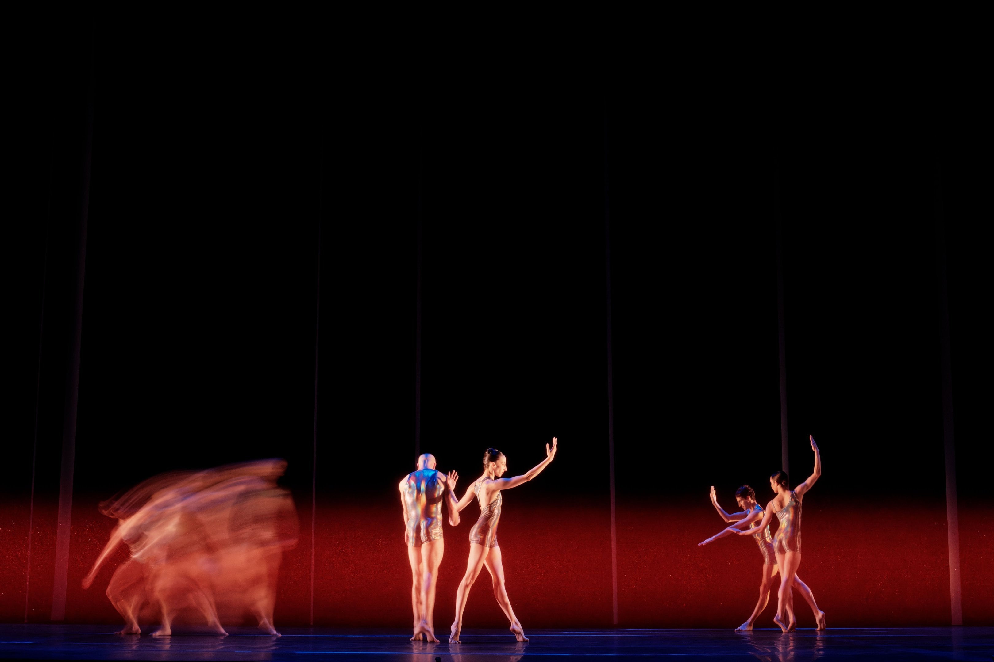 three dancers on a black background with a horizontal red light