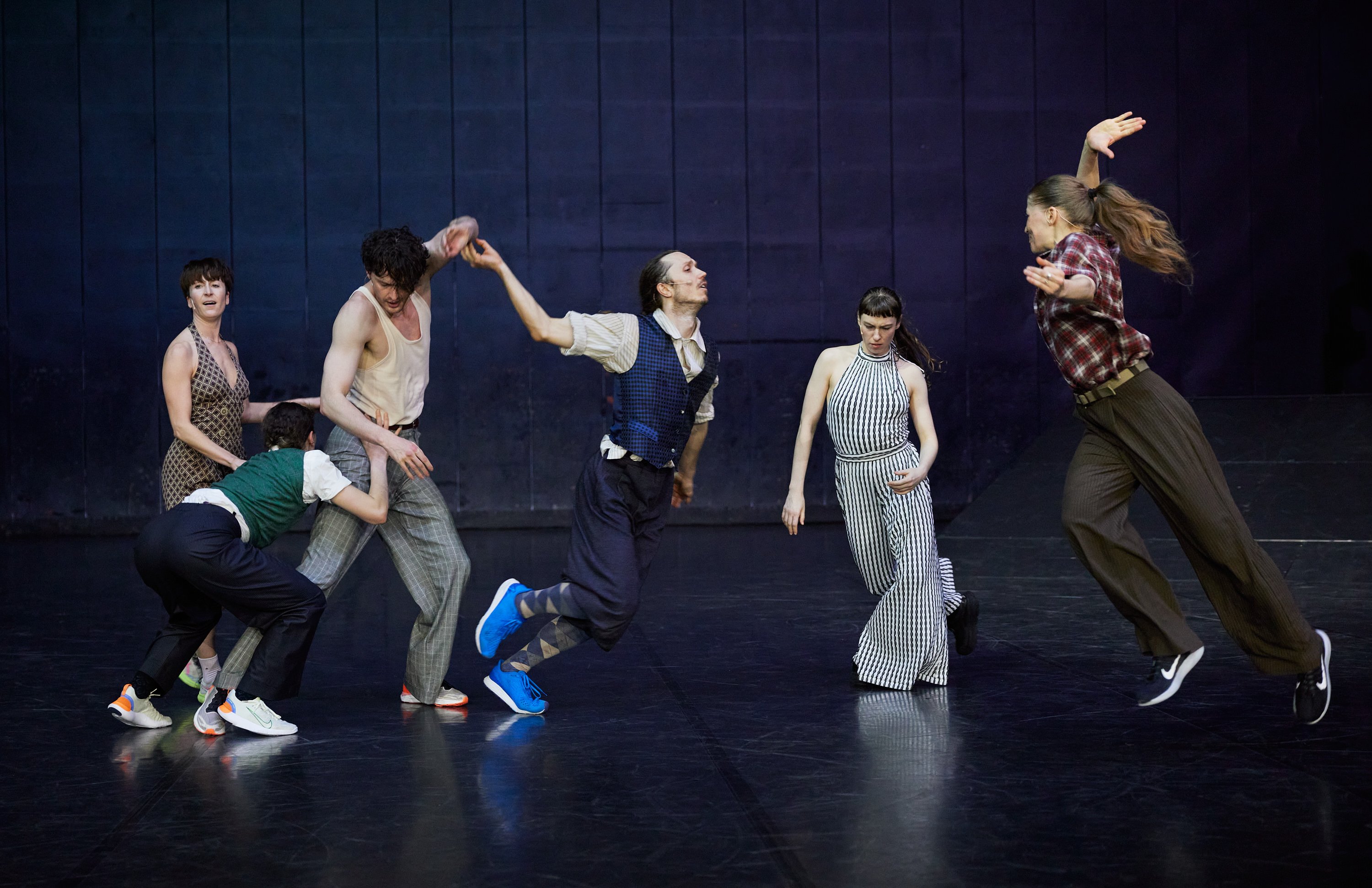 Six dancers, including two running, on a navy blue background