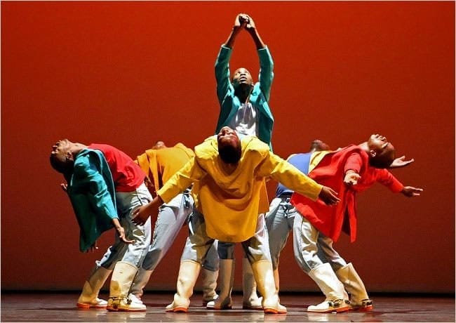 A group of dancers performing in front of a red background.