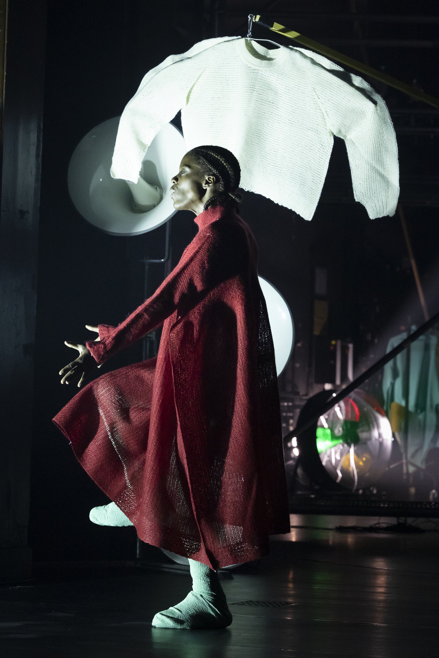 Danseur vêtu d'un long manteau rouge fluide, un pul en tricot blanc taille xxl en arrière plan