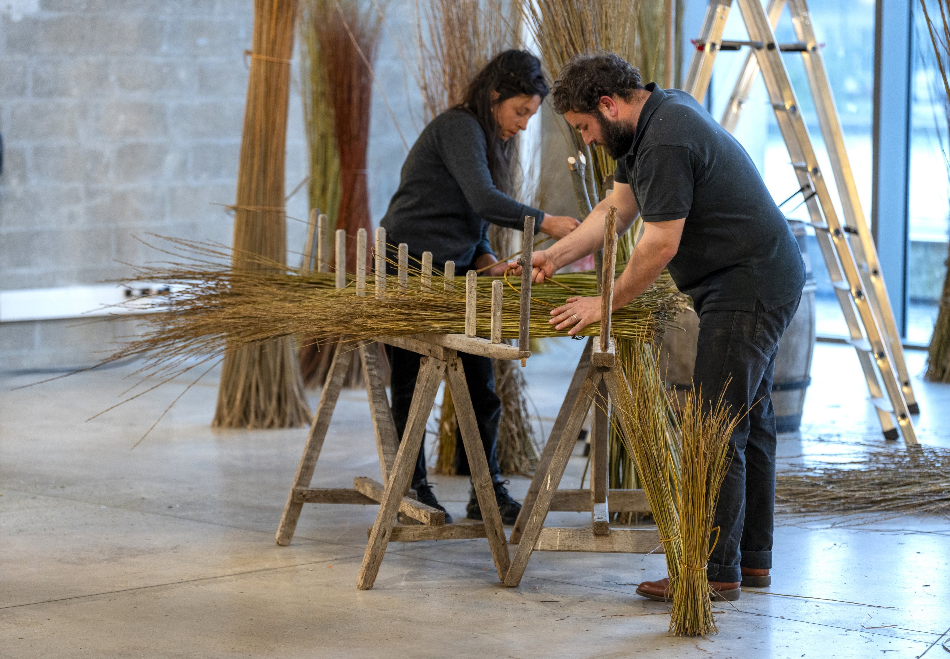 un homme et une femme travaillant des herbes sèches sur un établi 