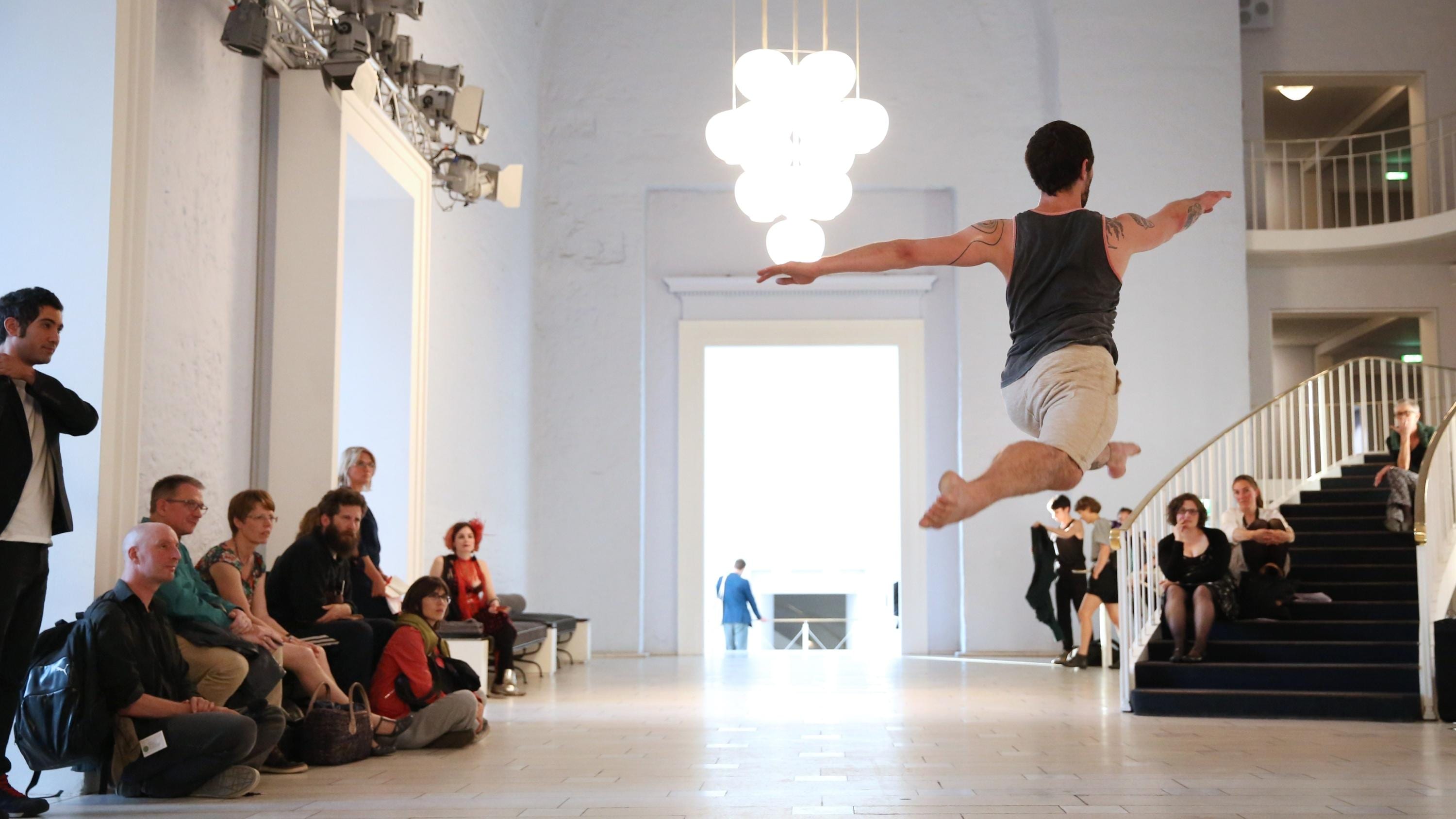 Boris Charmatz作品《20 danseurs pour le XXe siècle》中被观众围绕，正在全劈叉大跳的舞蹈演员背影
