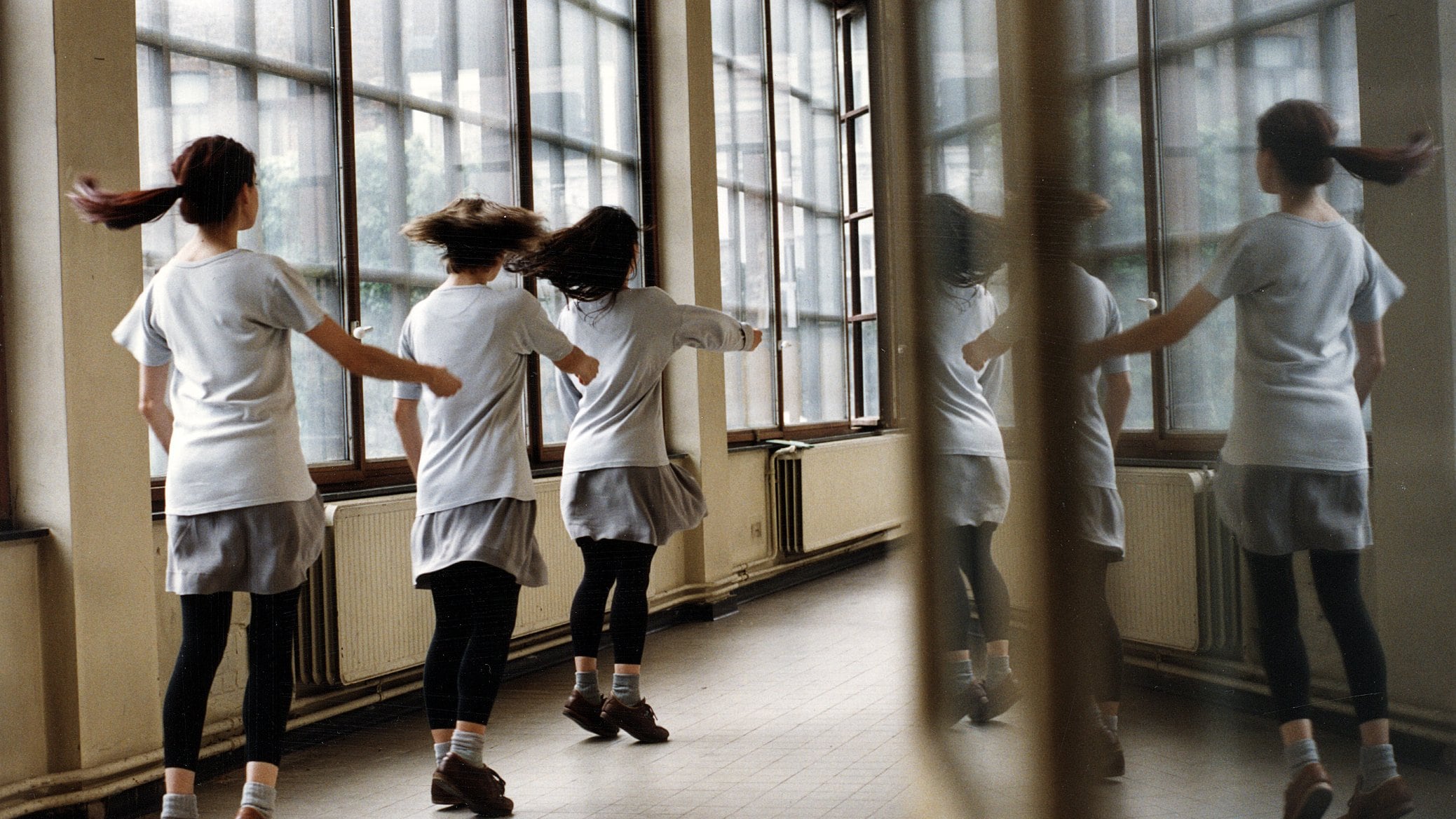 3 filles dansant en ligne devant un fênetre