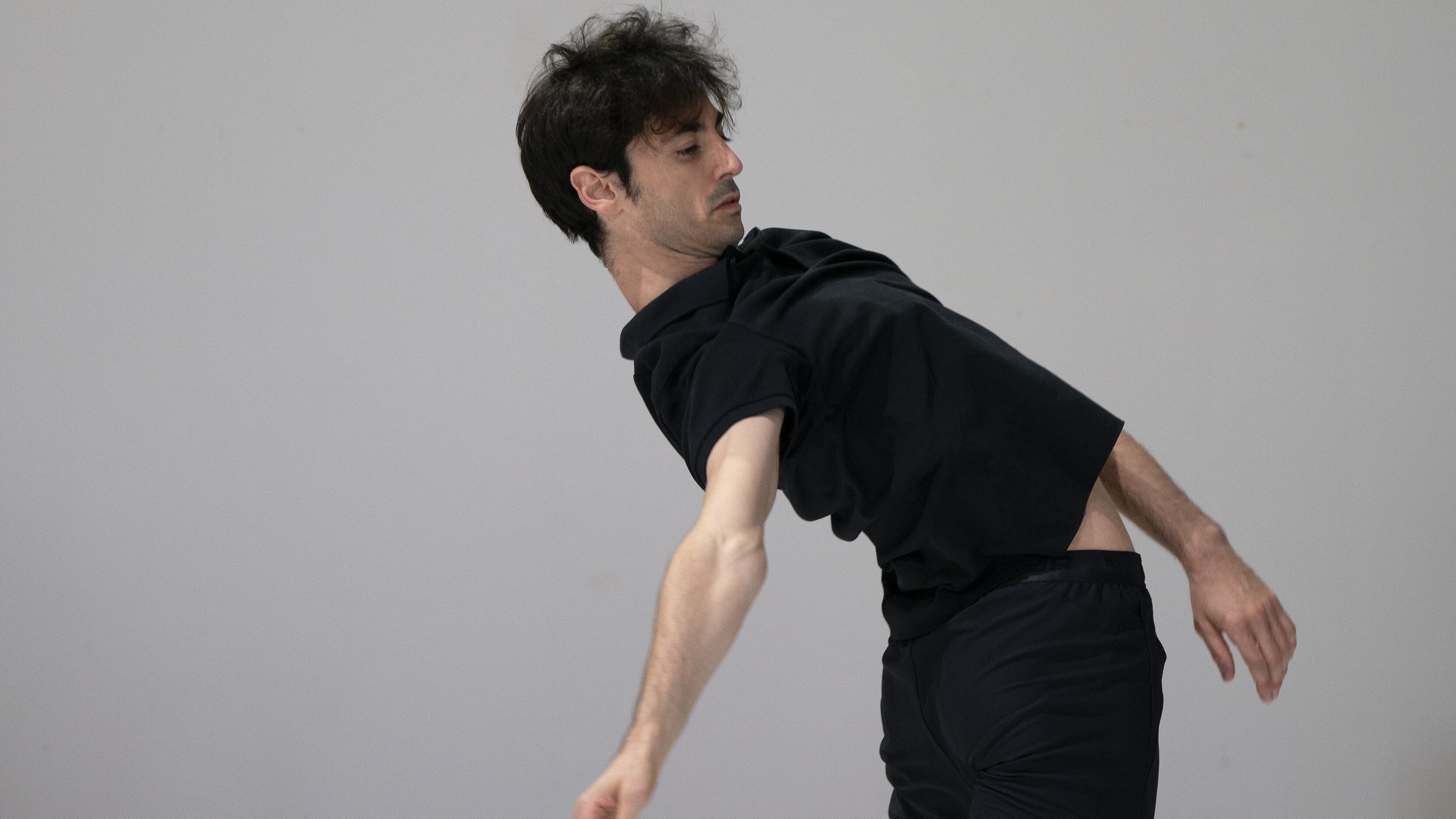 un danseur habillé en noir devant un mur gris se penchant en arrière