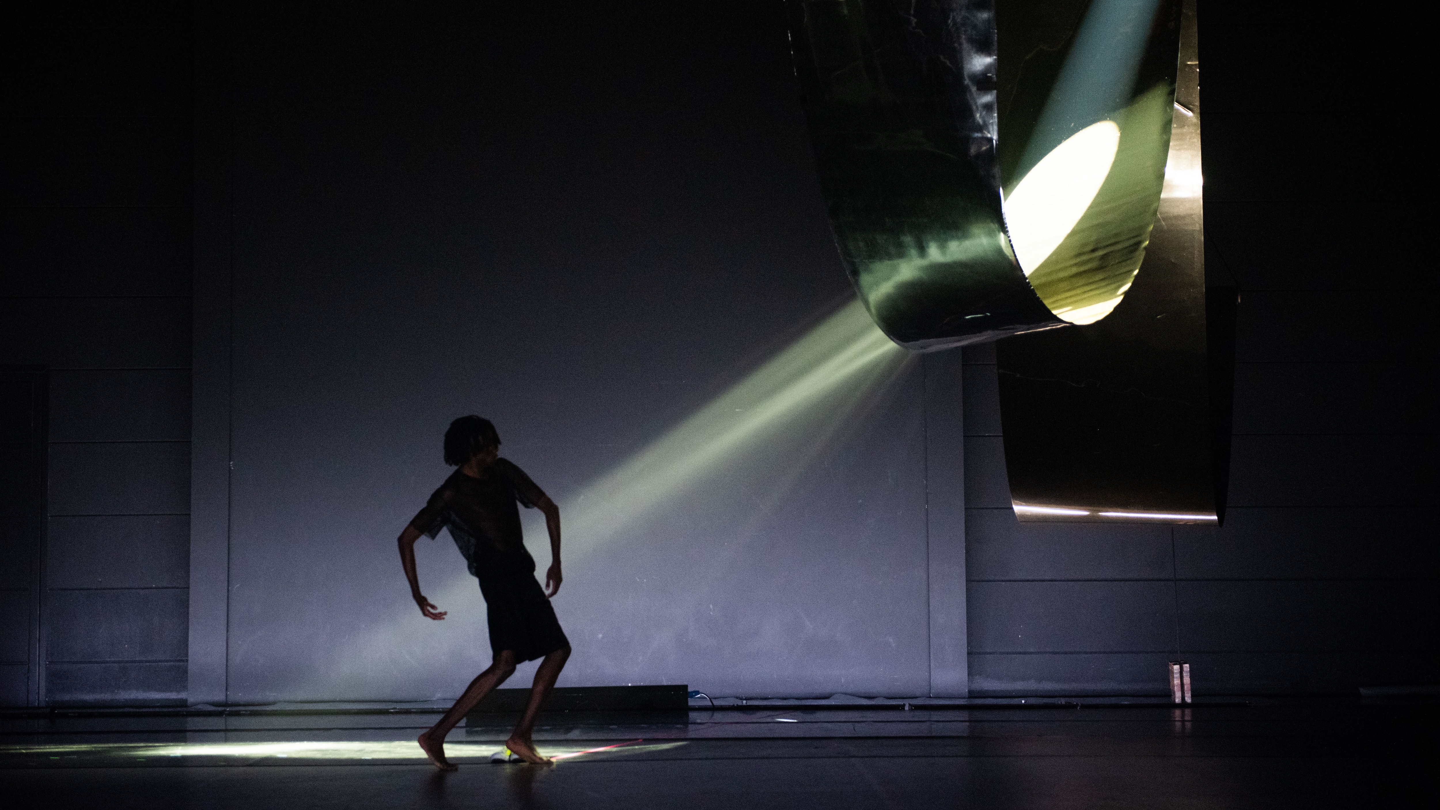 Danseur de profil sur une scène sombre face à un structure diffusant un rai de lumière