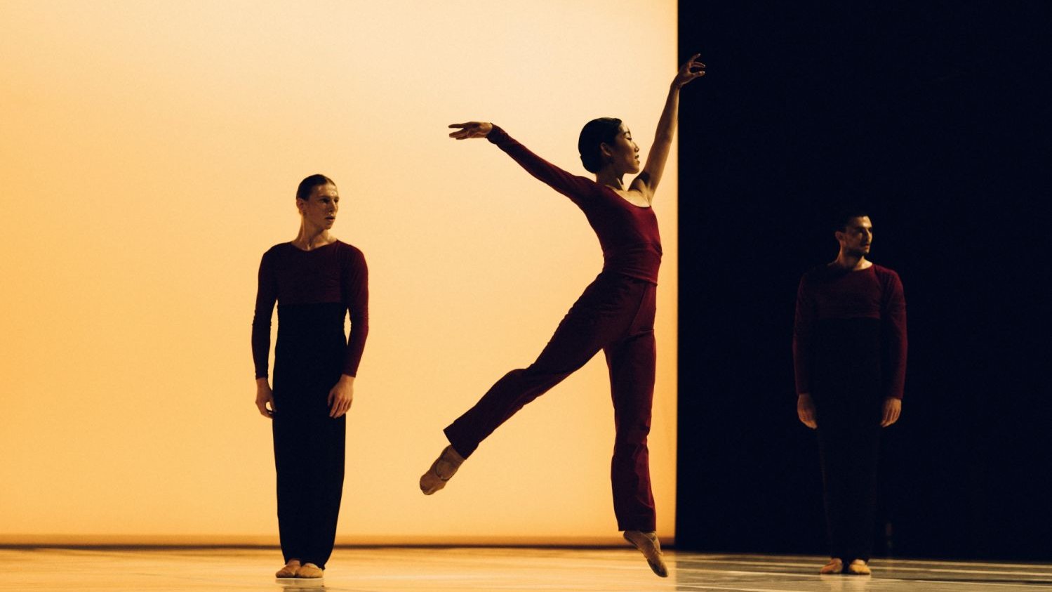 Leaping dancer in front of two static dancers on-stage 