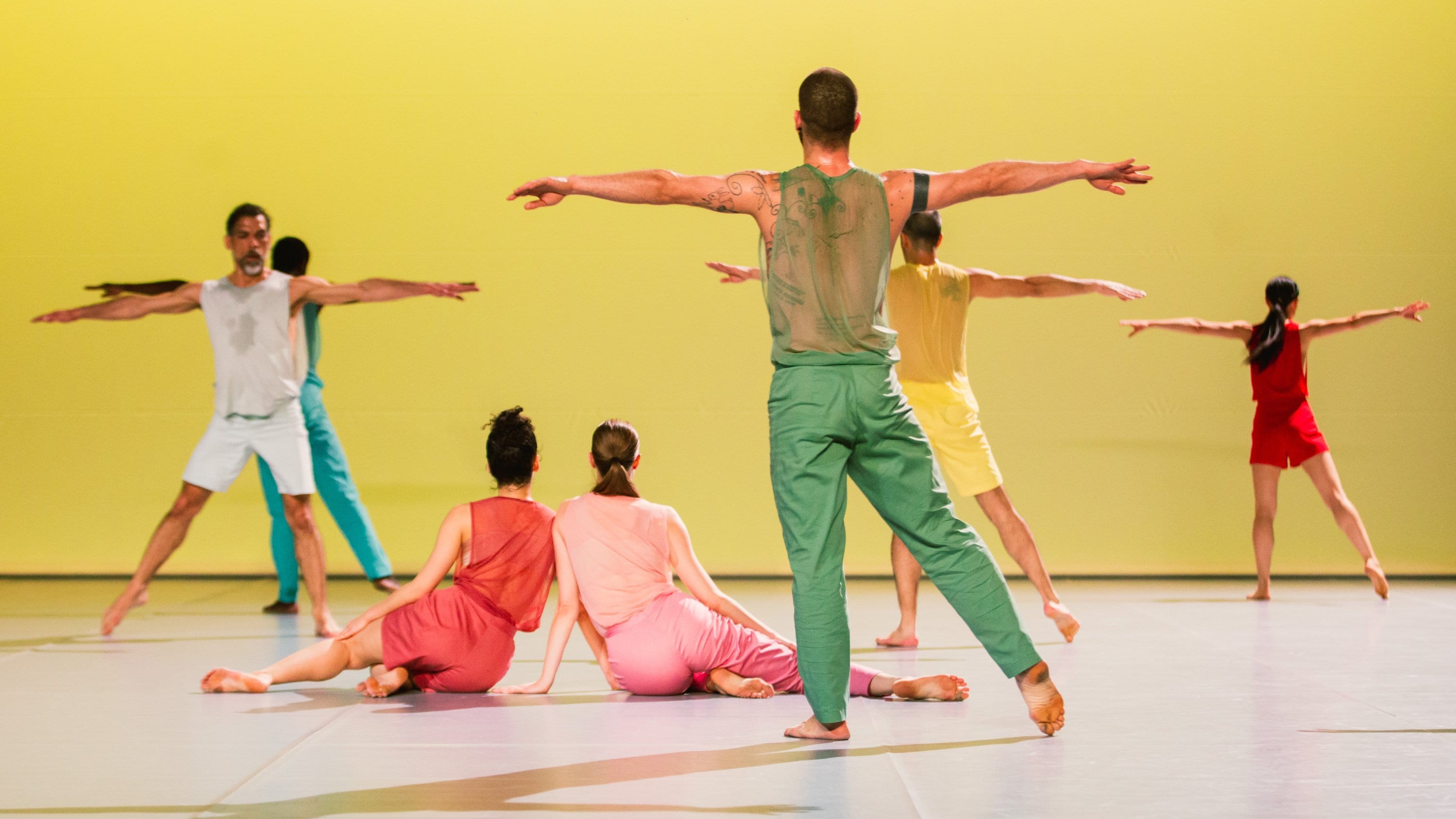 colorfully dressed up dancers on facing a yellow wall 