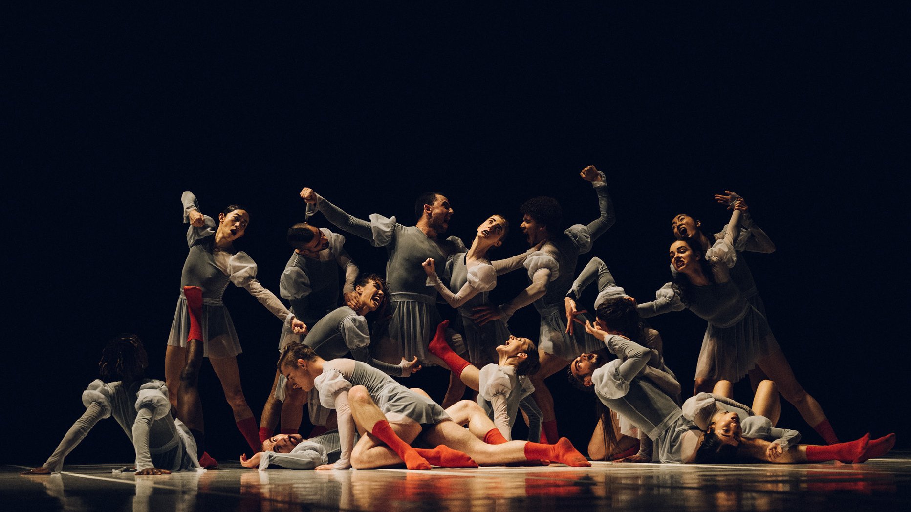 Group of dancers on-stage dressed in gray, with red socks