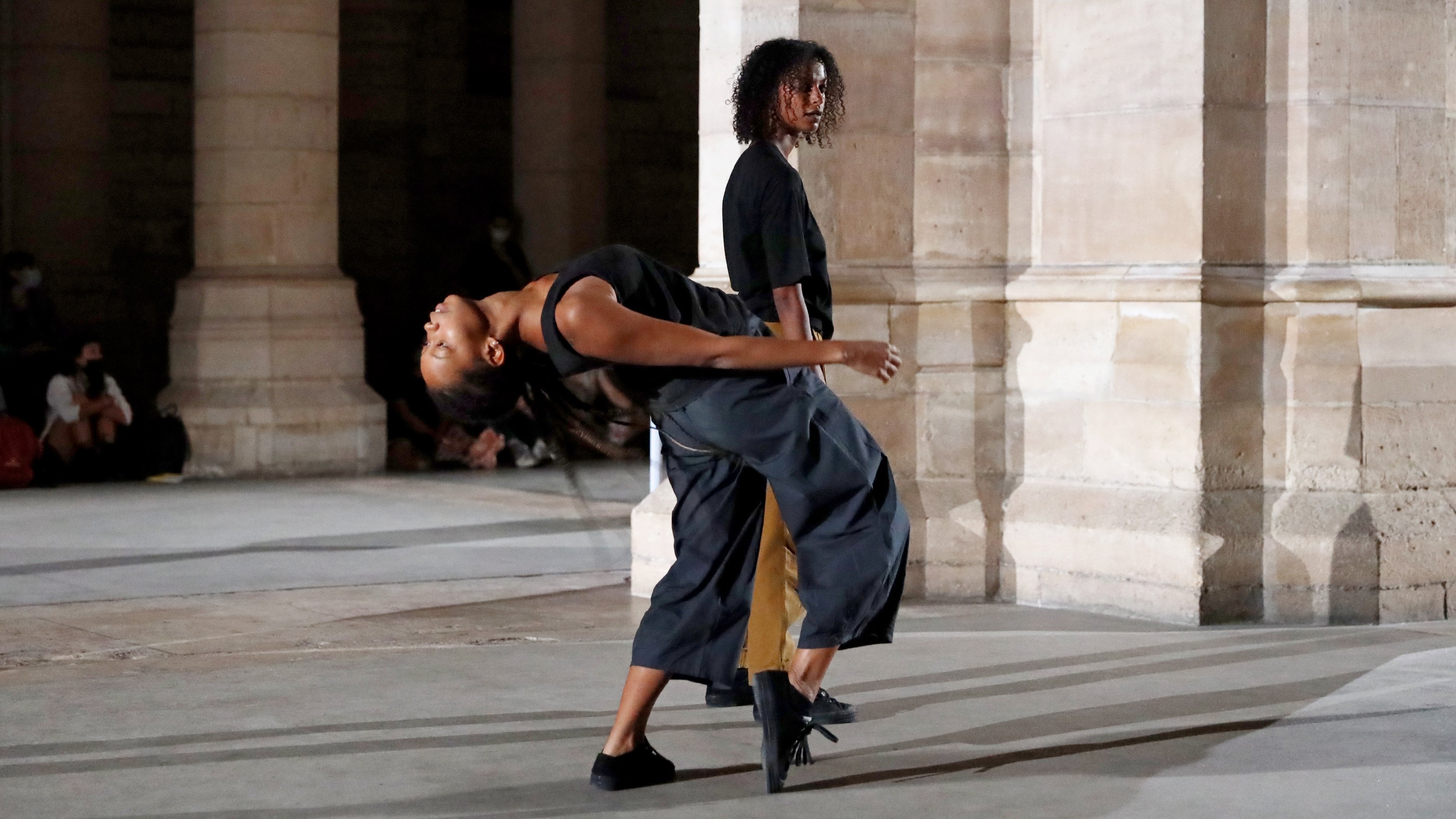 Un danseur debout derrière un autre danseur penché en arrière dans un espace avec des piliers