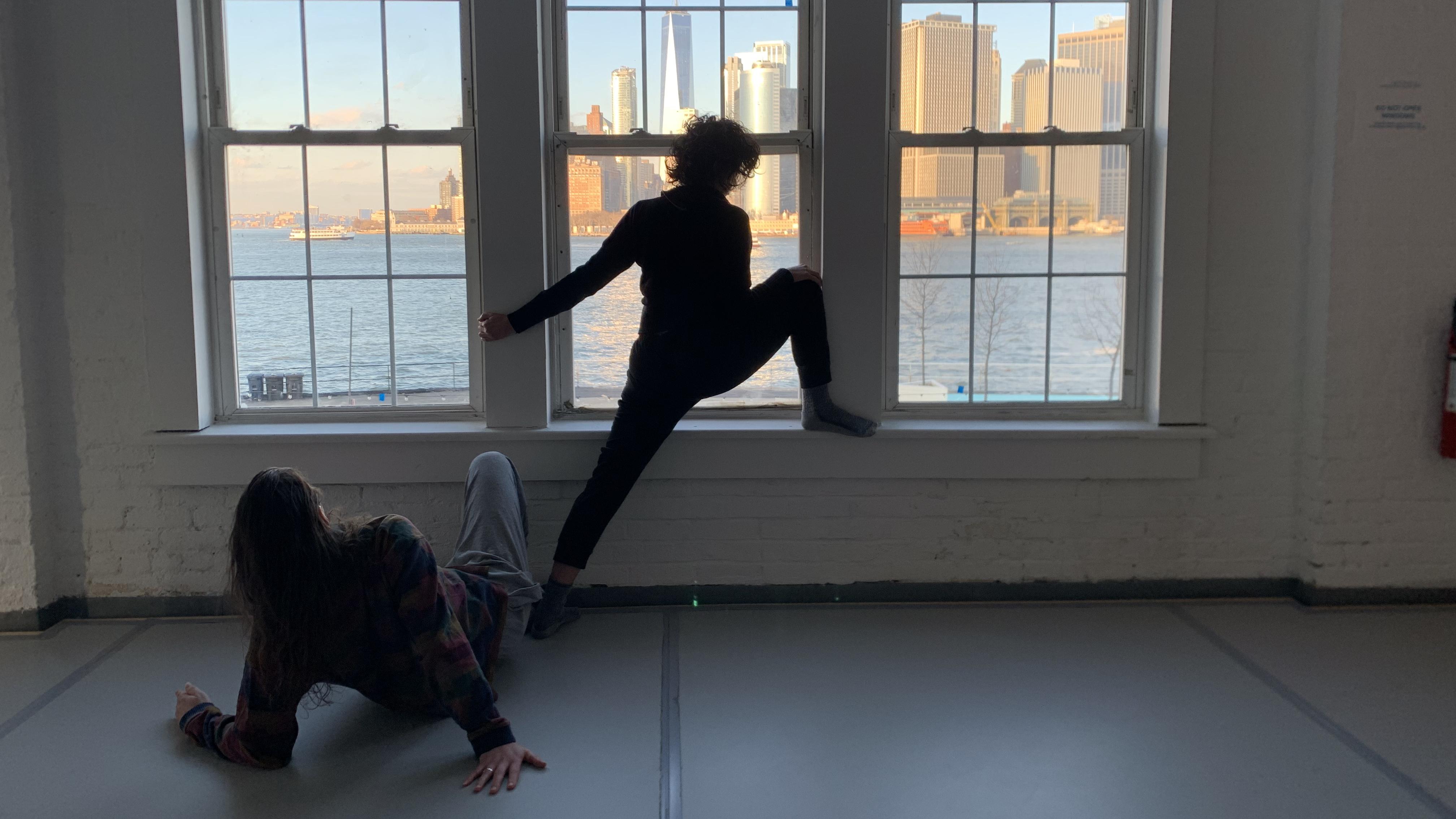 「兩位舞者在俯瞰紐約風景的窗前伸展身體」