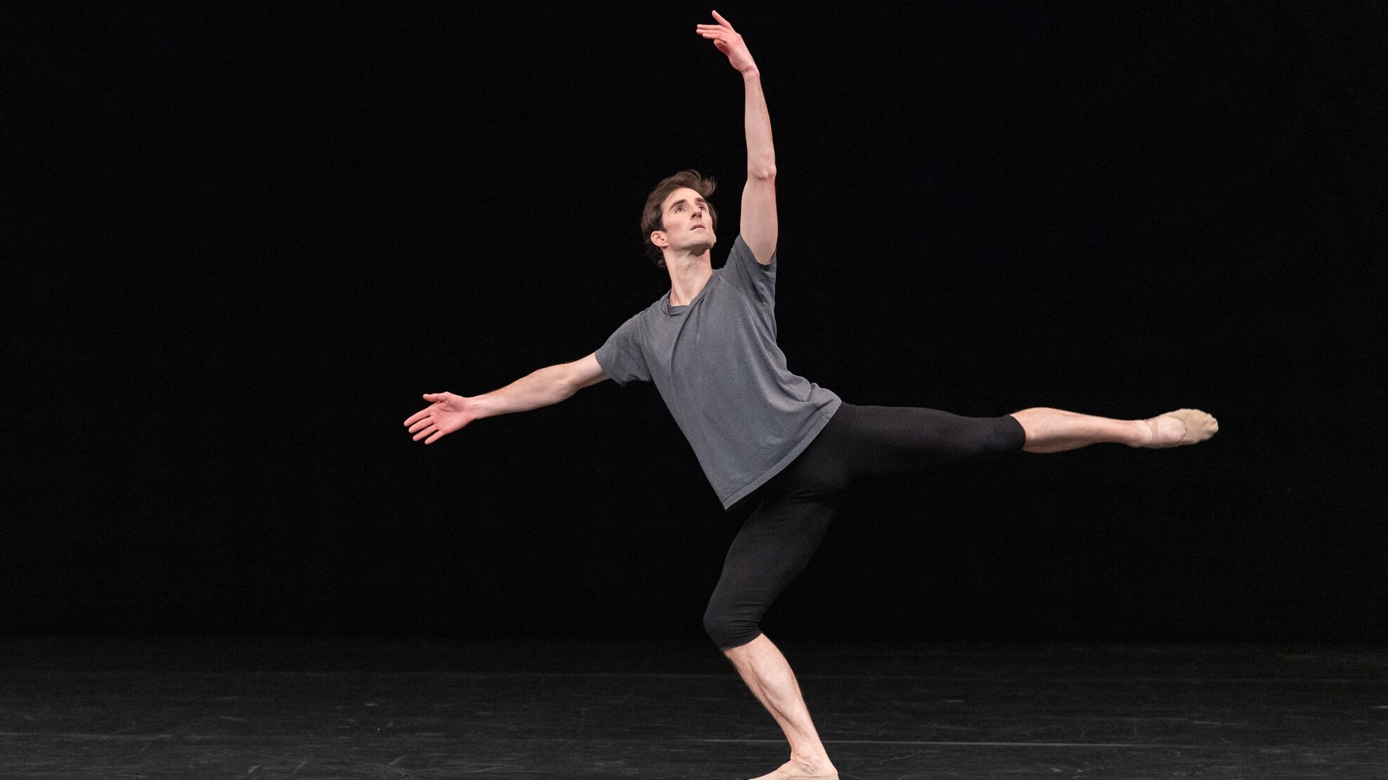 un danseur en arabesque regardant vers sa main lévée