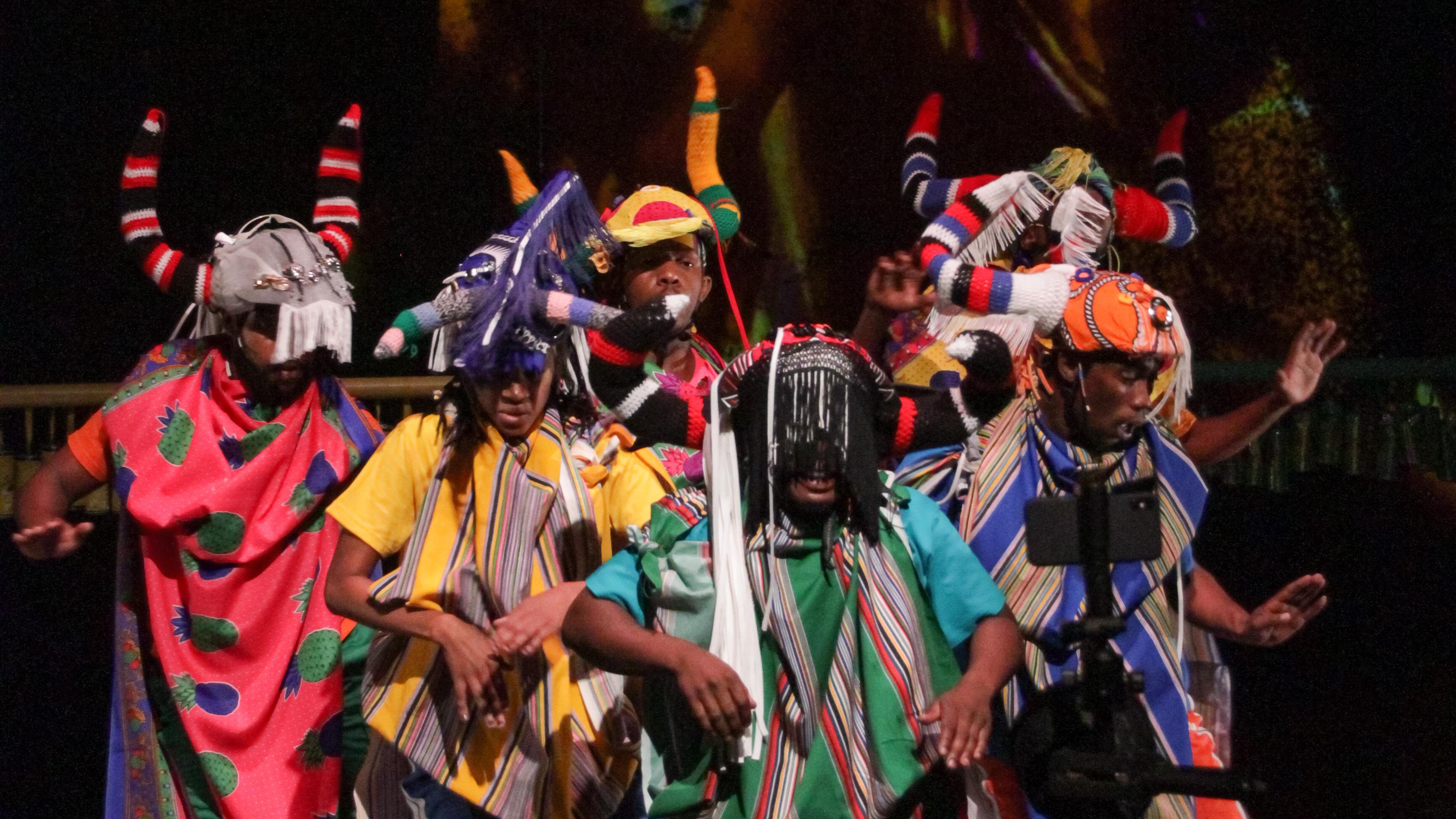 danseurs vêtus de tissus imprimés colorés et de coiffes sur une scène sombre