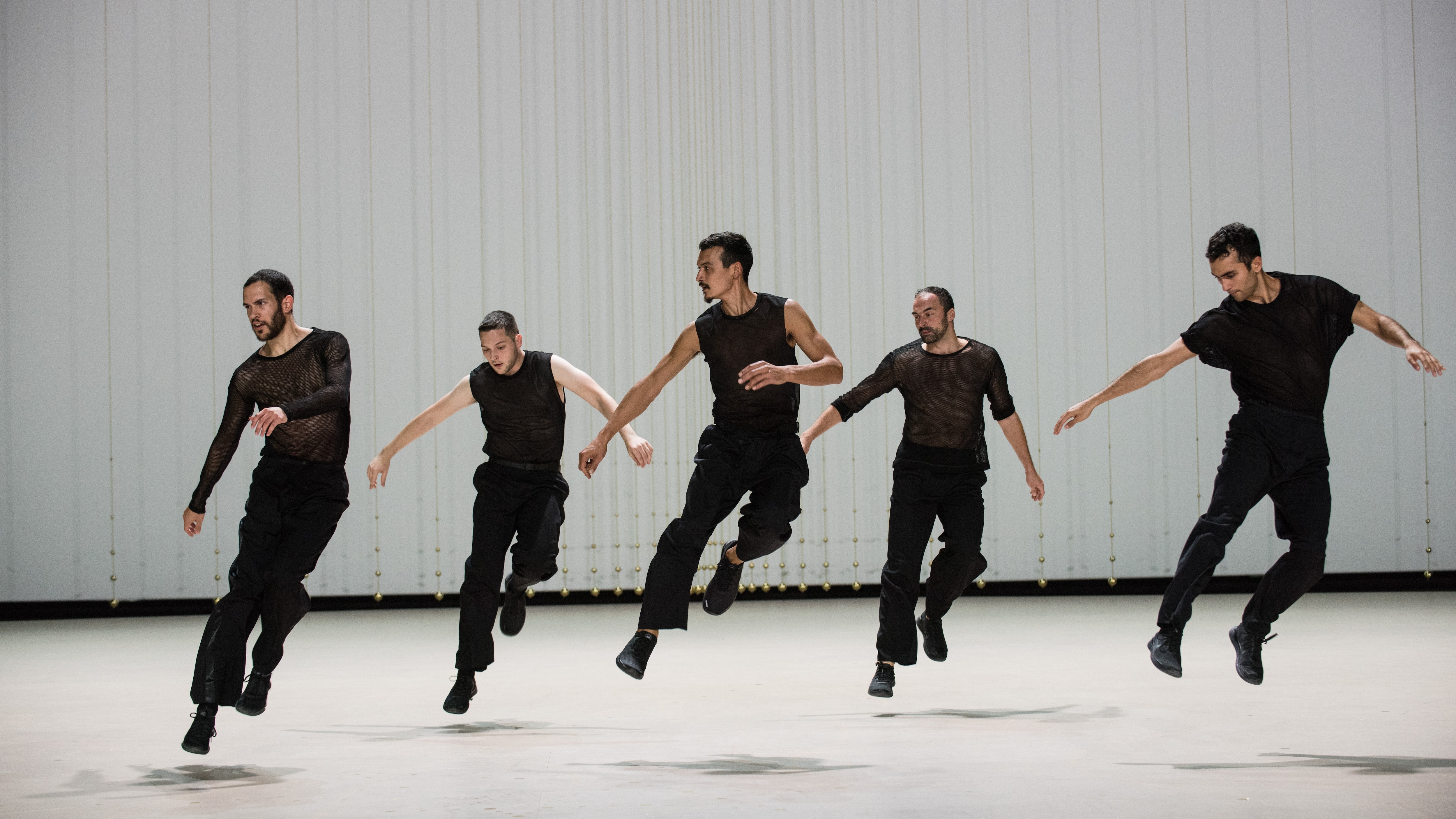 Five dancers wearing black, jumping