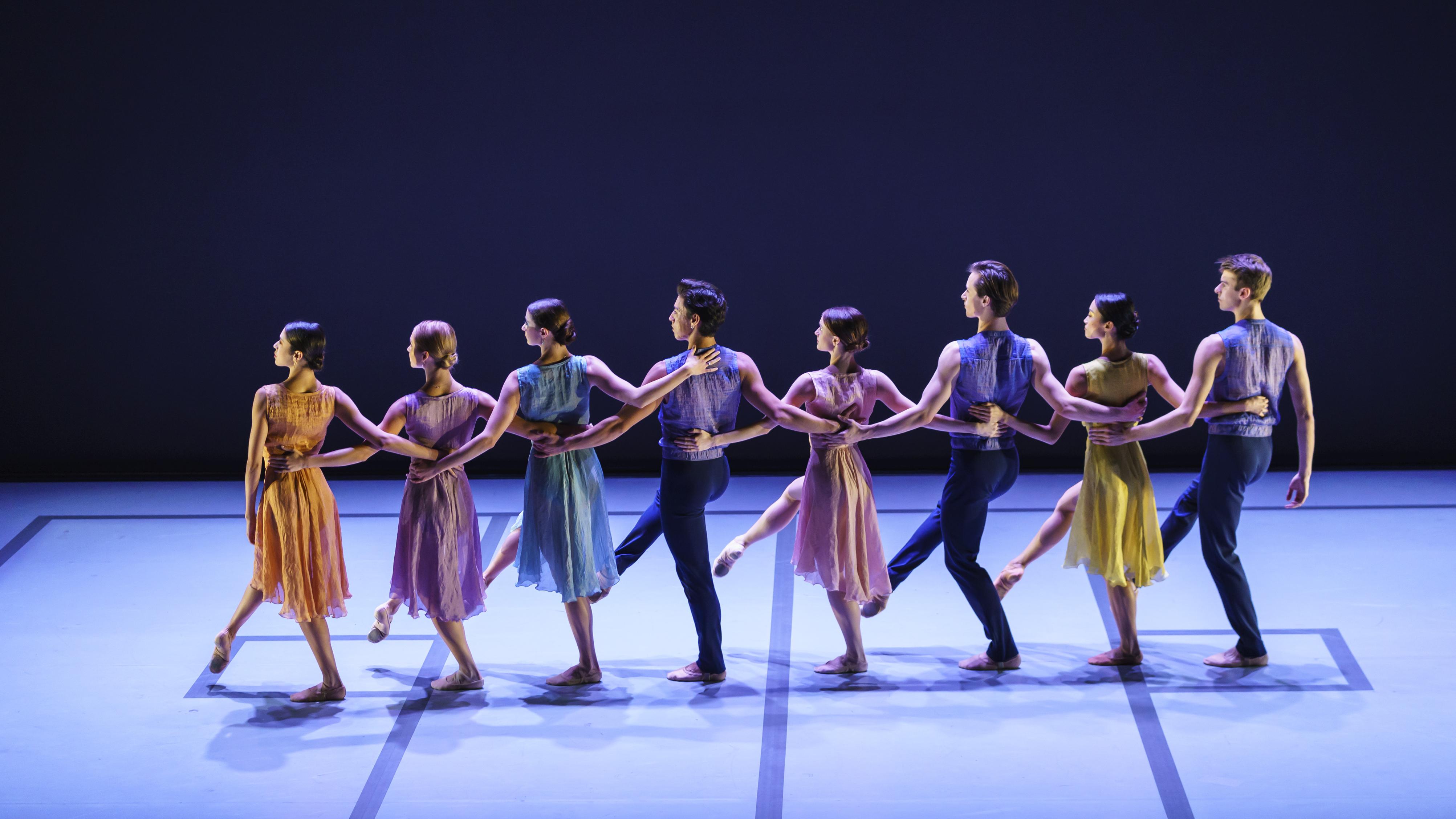 Dancers in line facing the back of the stage, holding each other by the waist