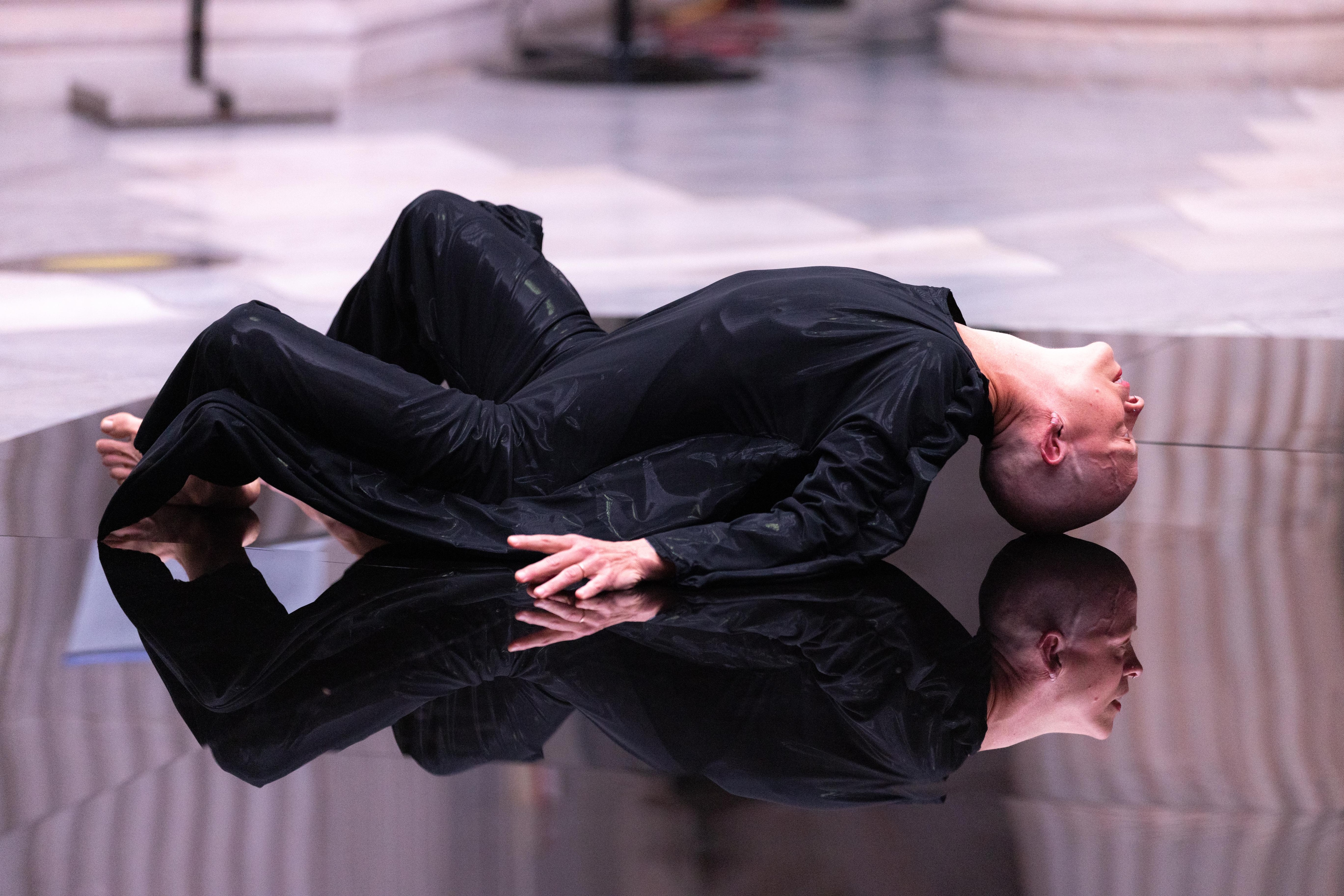 Bald woman dressed in black, lying on a reflective floor