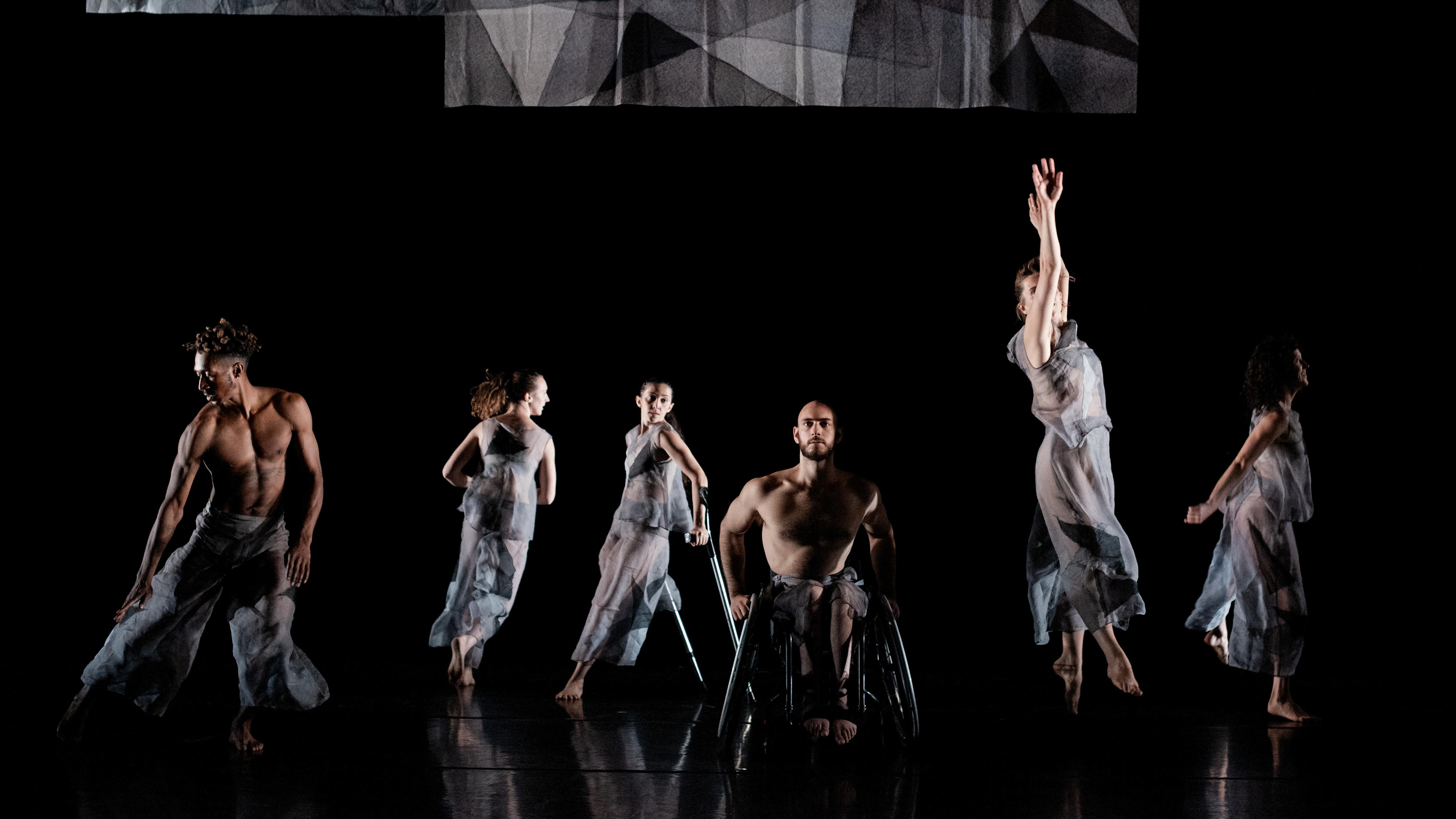 6位舞者身穿灰色透明服装，在黑色舞台上起舞