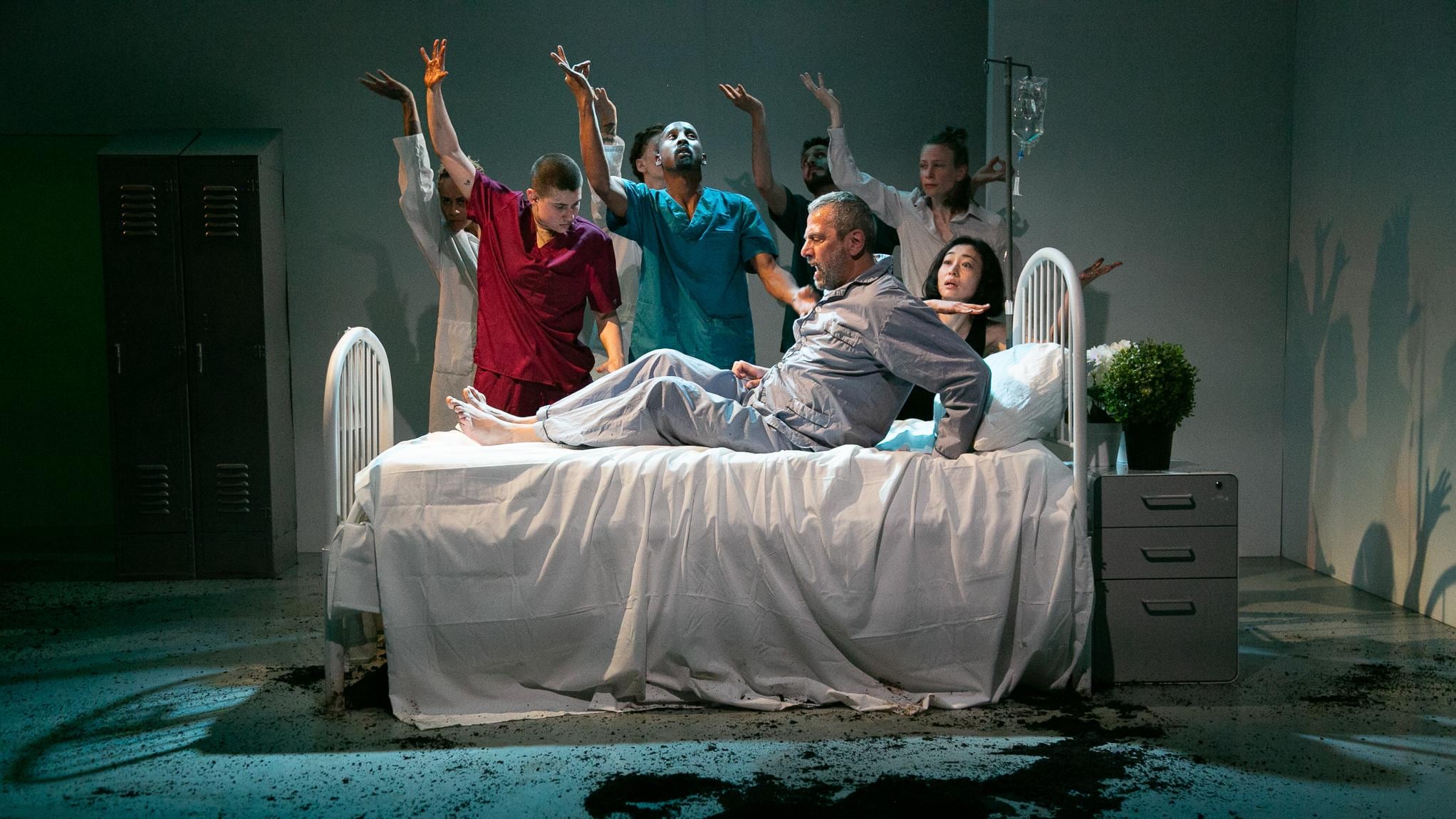Dancers dressed as caregivers, surrounding a man on a hospital bed 