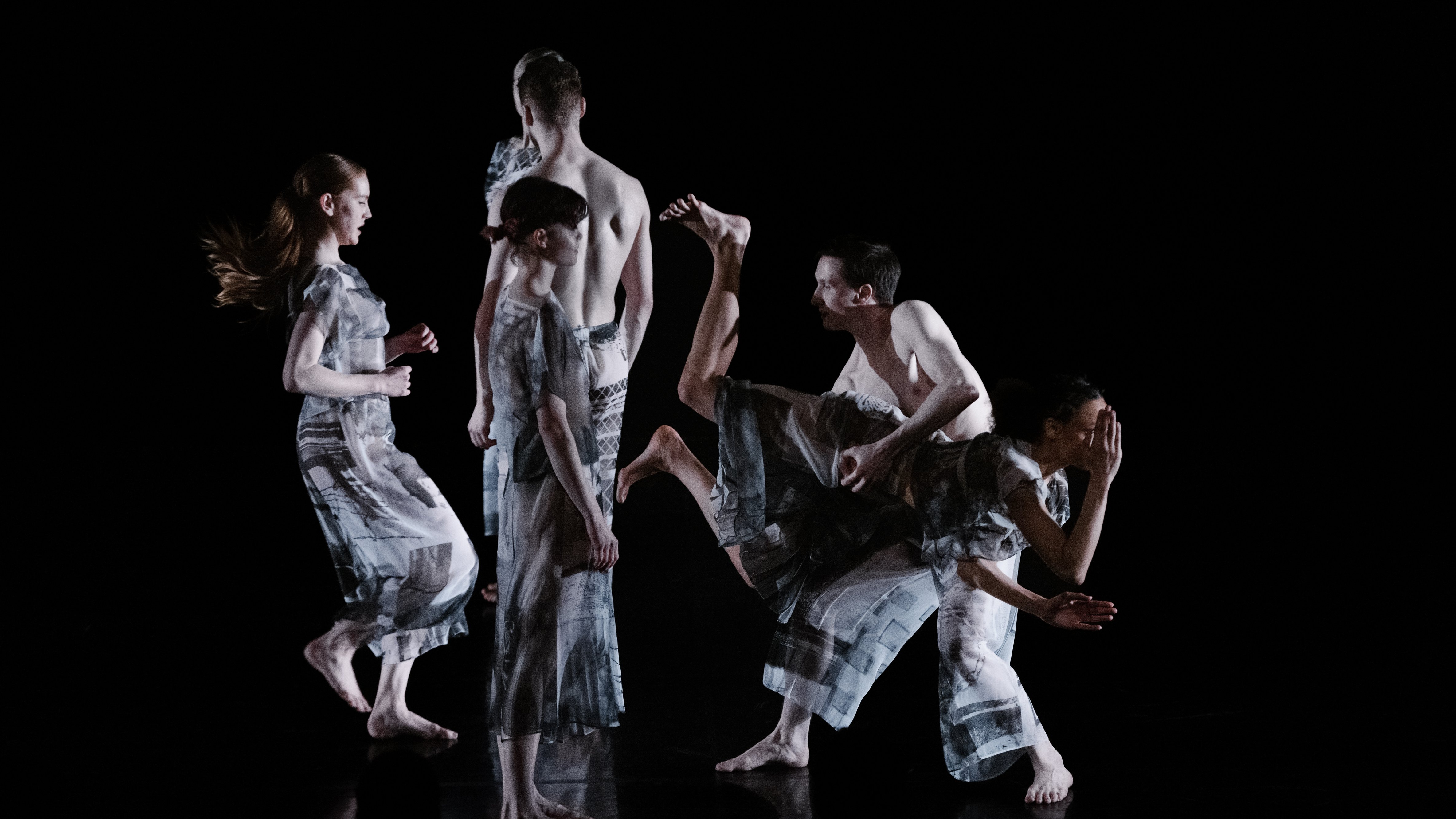 Dancers wearing grey on a dark stage