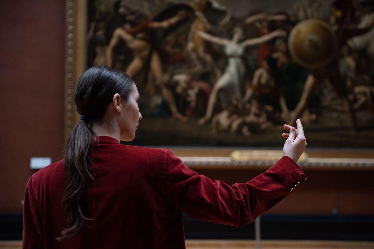 danseuse vue de dos, portant une veste rouge, le visage tourné vers le bras droit levé