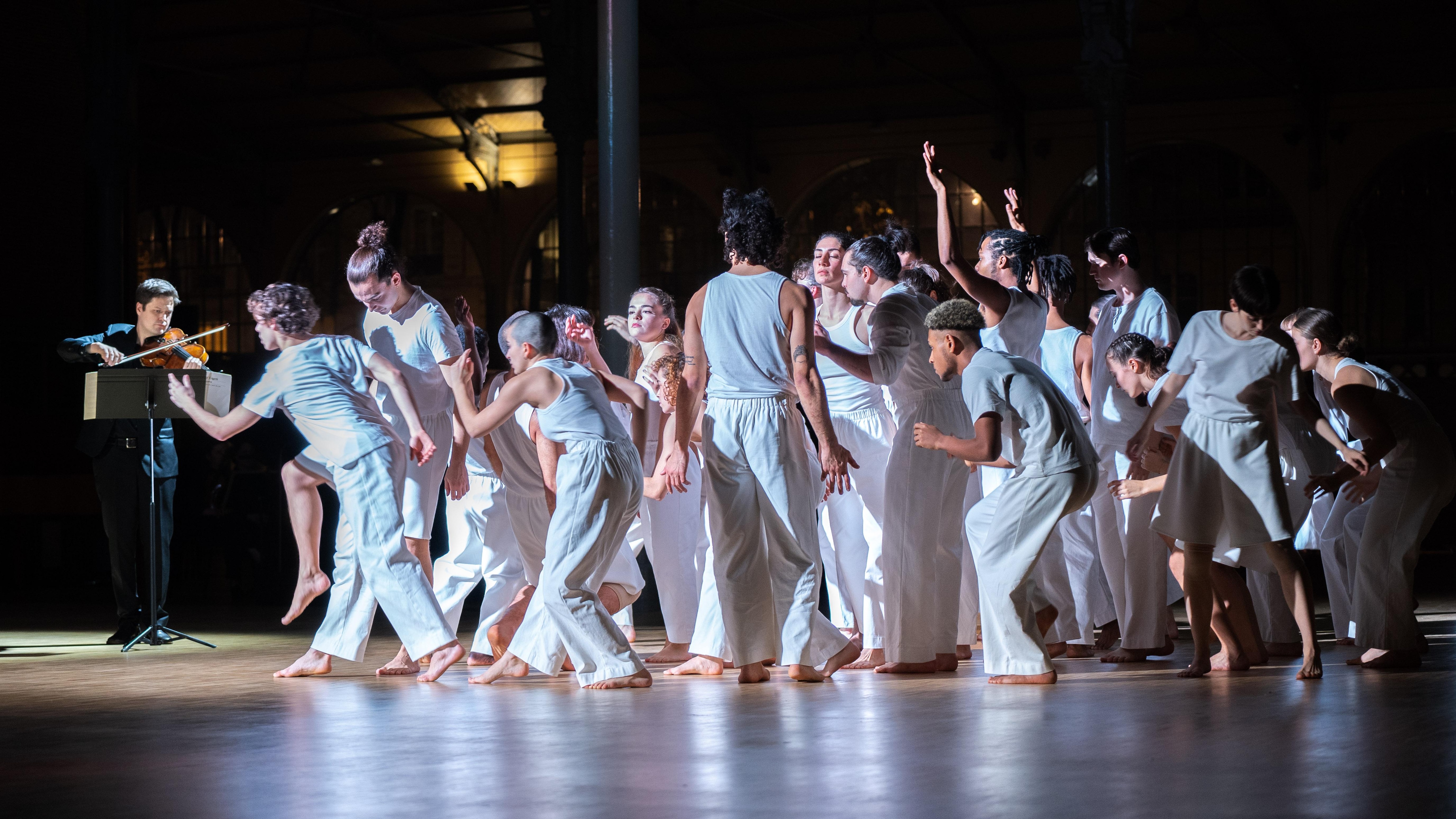 Dancers standing in white clothes, grouped together, making desynchronized movements.  
