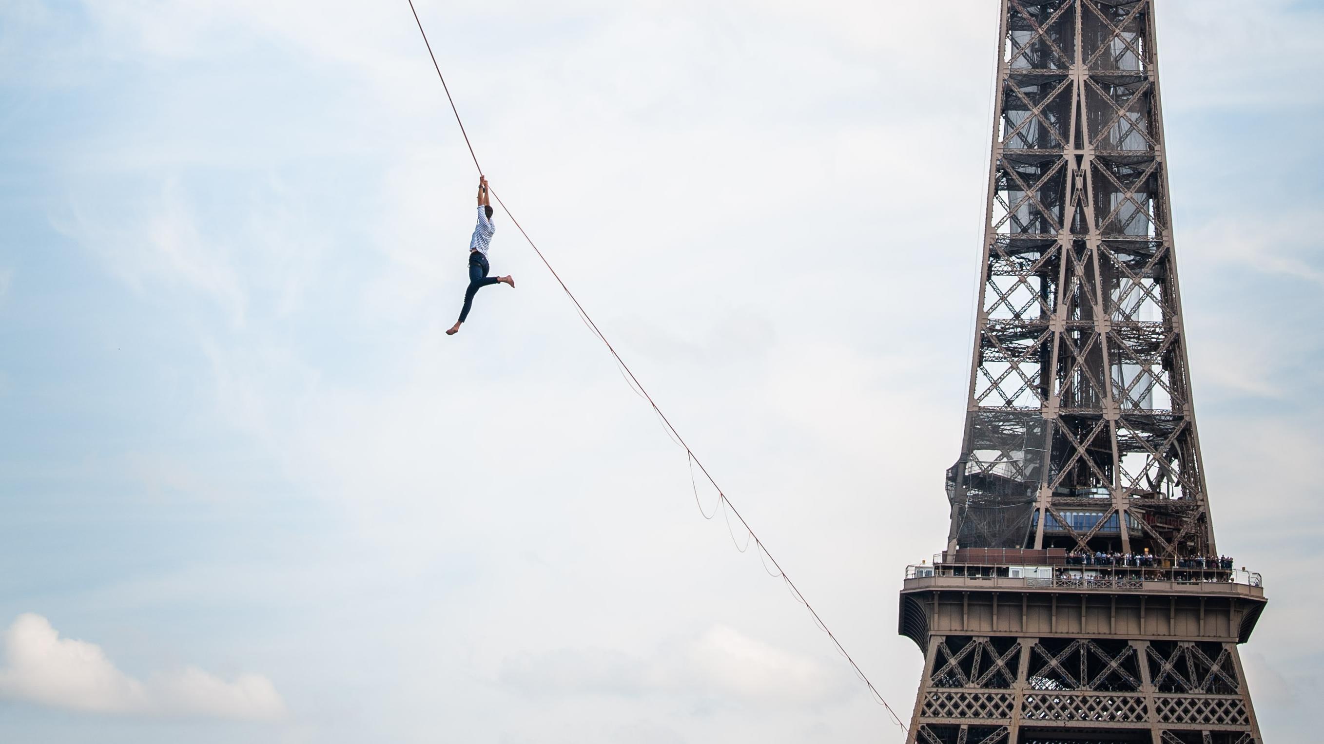 A tightrope walker hanging on a tightrope, next to the Eiffel Tower